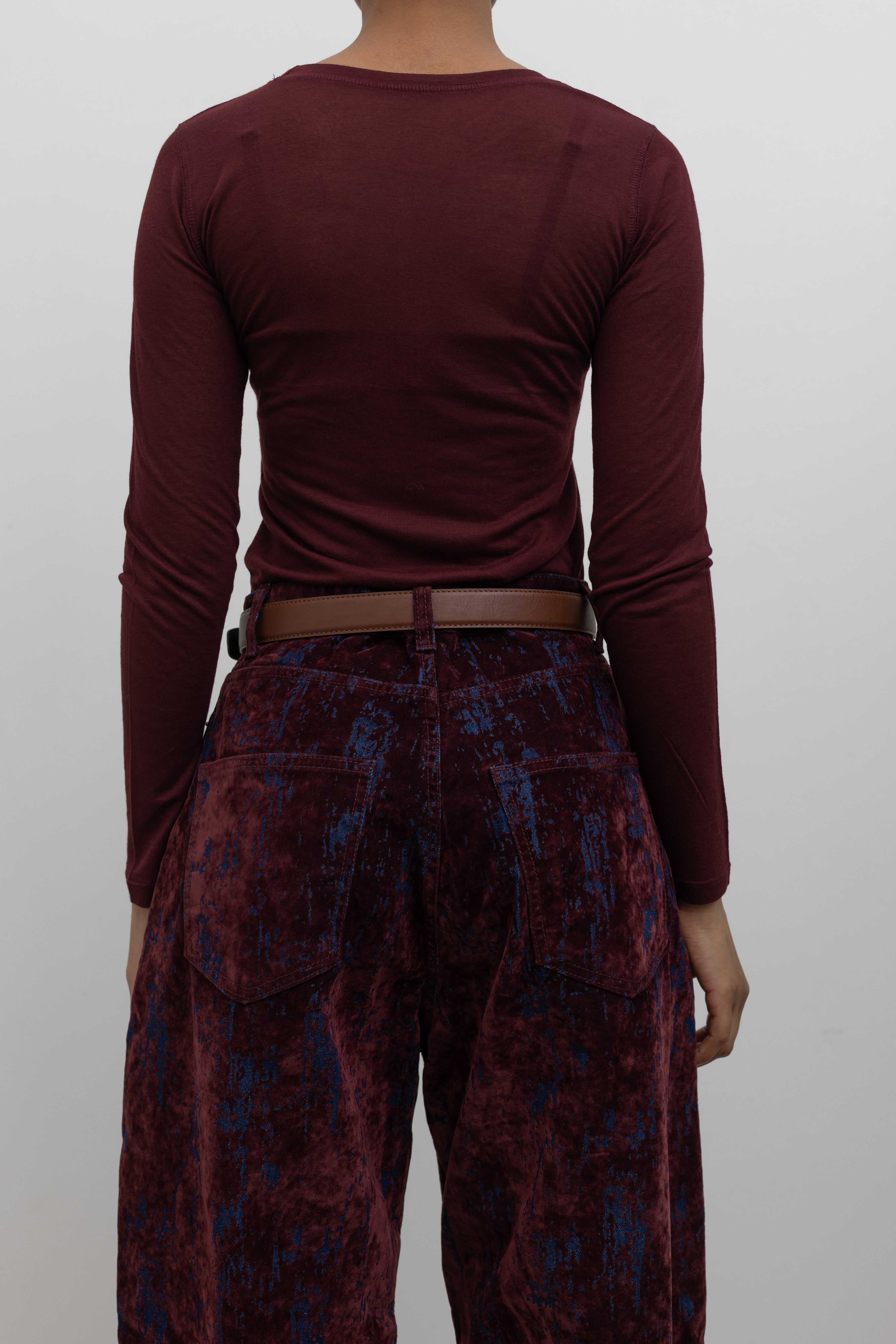 Back view of a woman wearing a capsule wardrobe essential accessory in a Collective brand classic brown leather belt made with a silver square shaped buckle at an Alas Eius store. 