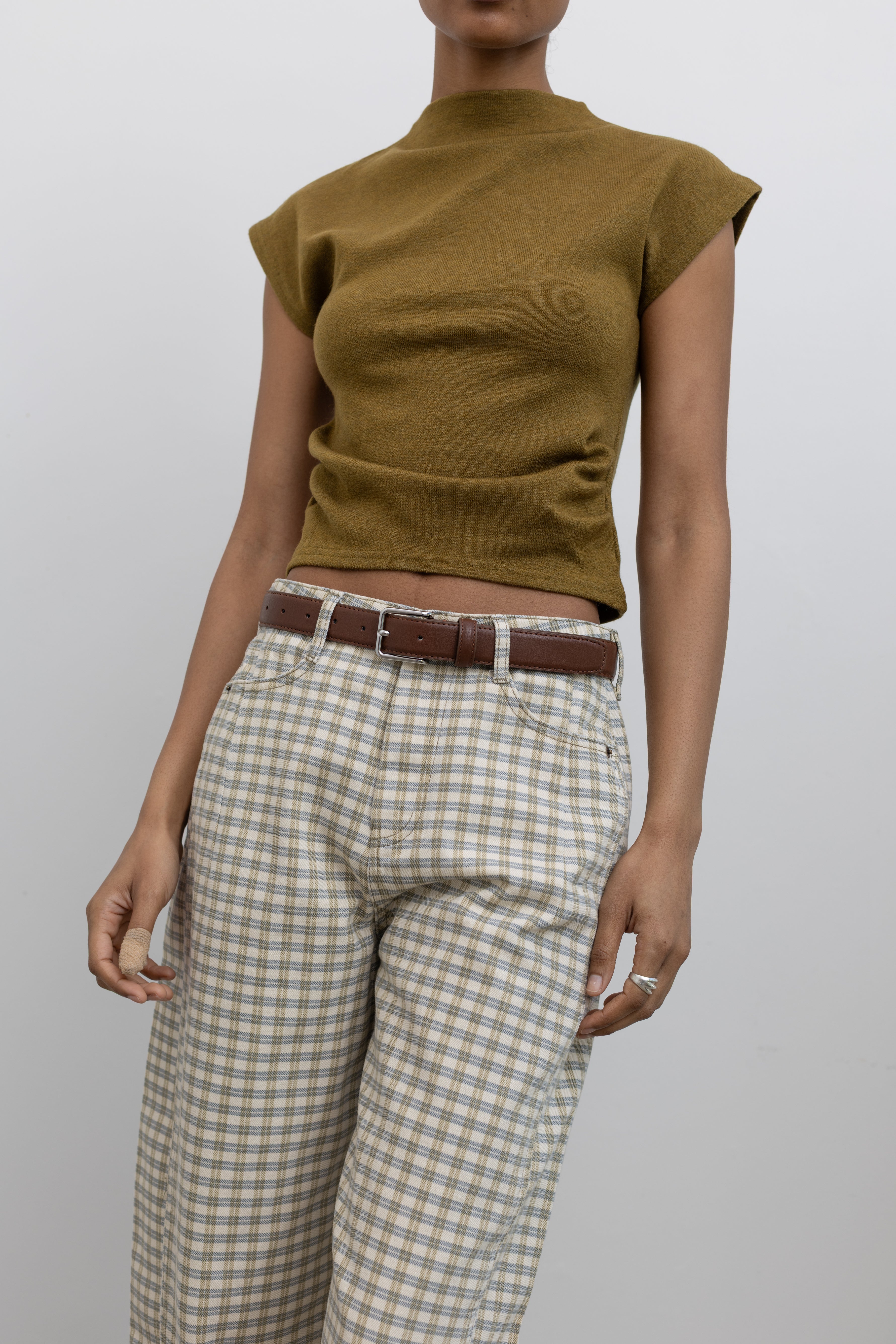 Woman wearing a capsule wardrobe essential accessory in a Collective brand classic brown leather belt made with a silver square shaped buckle at an Alas Eius store. 