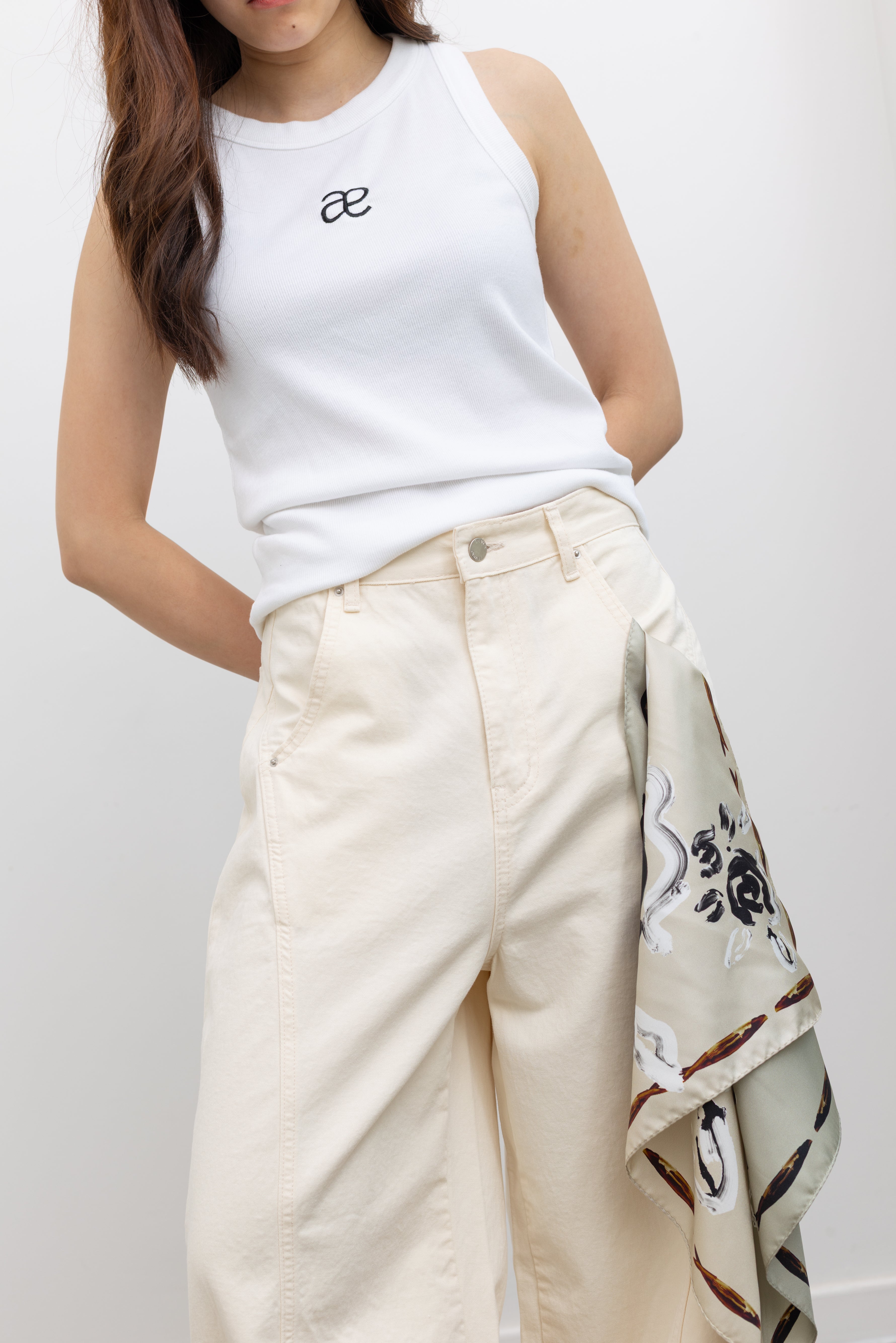 Model wearing relaxed yet chic summer fashion in Collective ivory heavy-weight cotton denim jeans with a structured wide-leg silhouette, curved paneling, and relaxed oversized fit paired with an Alas Eius label logo tank and Veja slide sandals at Alas Eius.