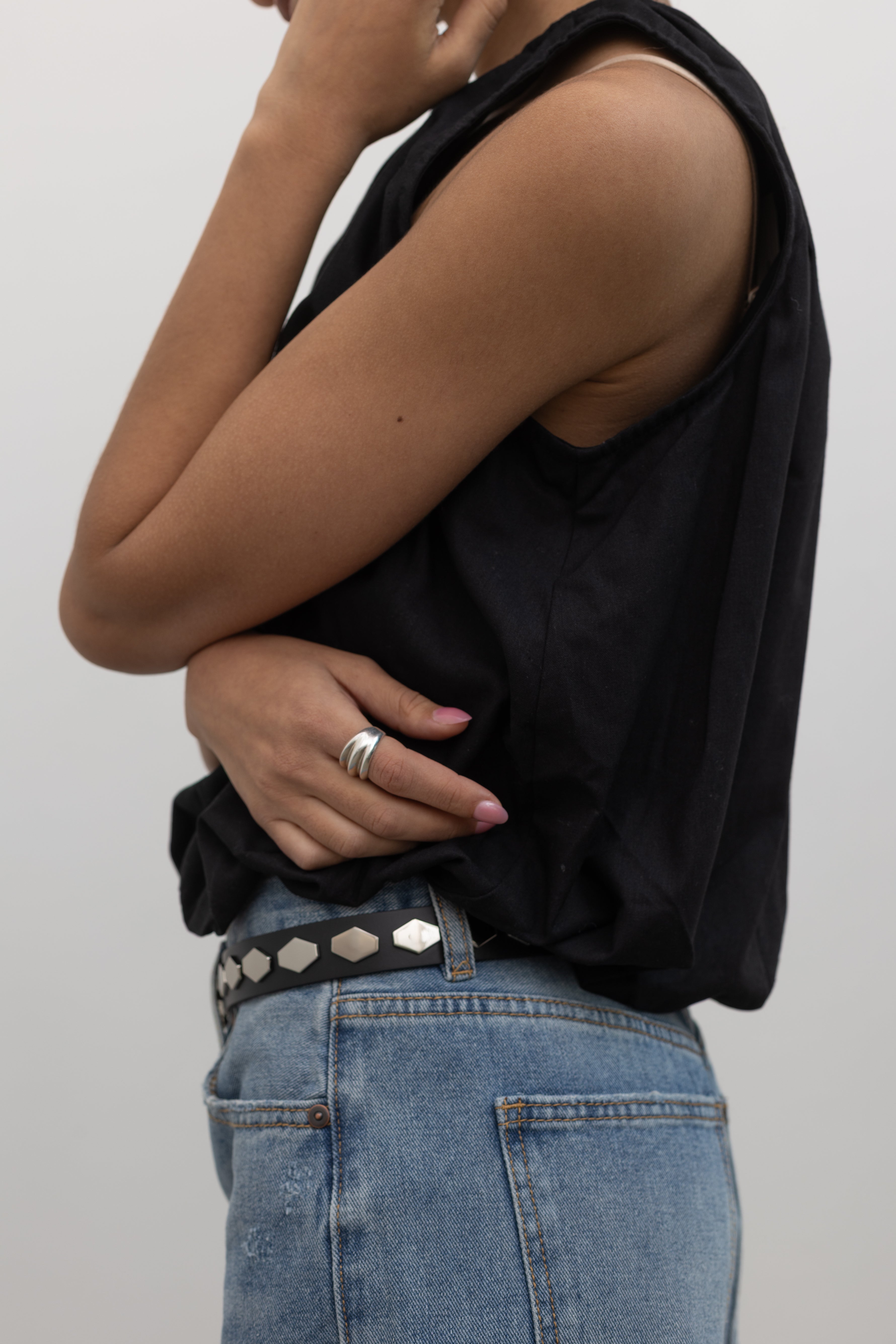Woman wearing an elevated classic essential accessory in a Collective brand Italian black leather belt with shiny silver honeycomb shaped hardware paired with light wash denim jeans and a white crop top at Alas Eius. 