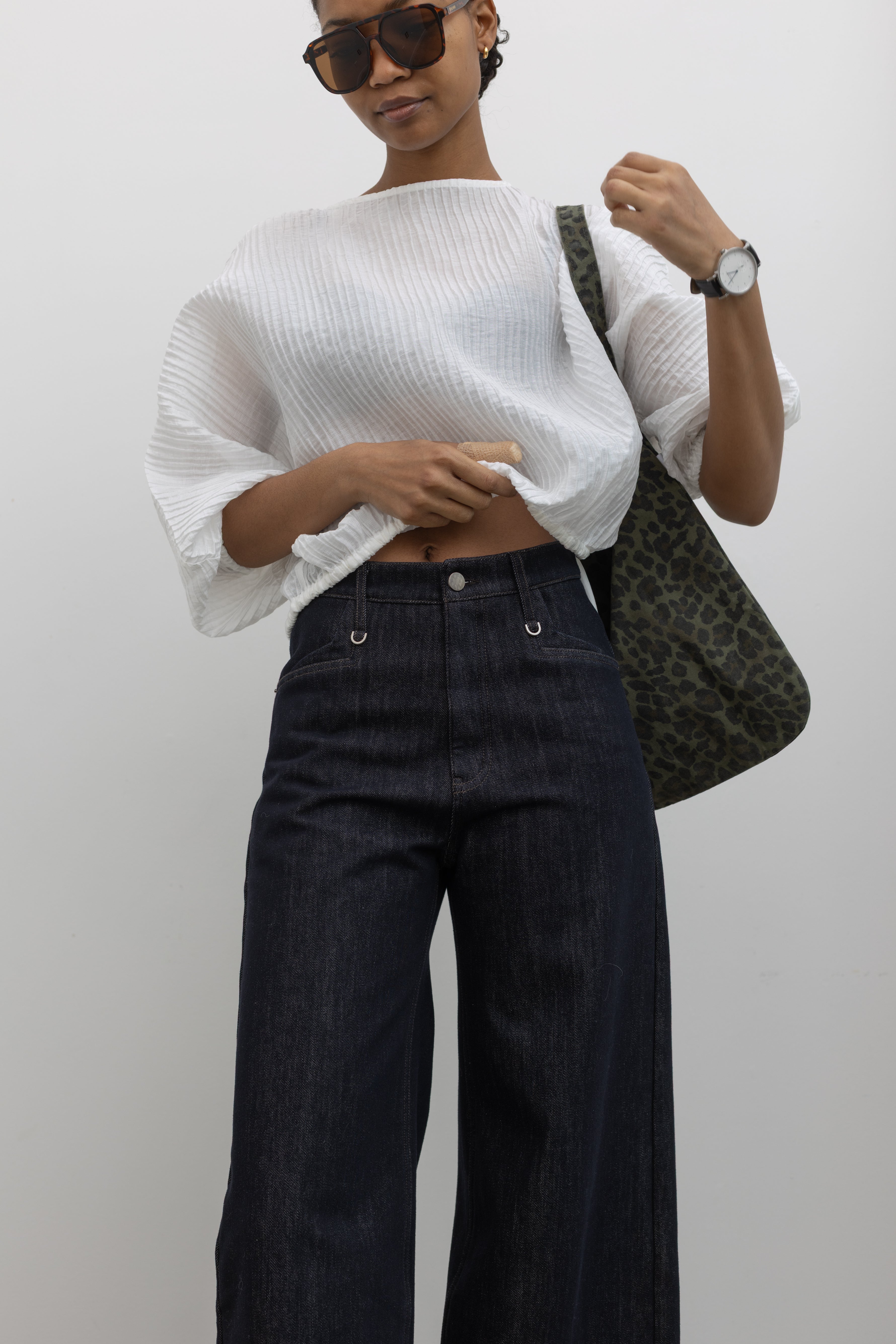 Close-up detailed view of a woman wearing Collective brand dark wash fleece lined wide-leg, high-rise jeans with squared off pockets with silver hardware and a white top at Alas Eius.