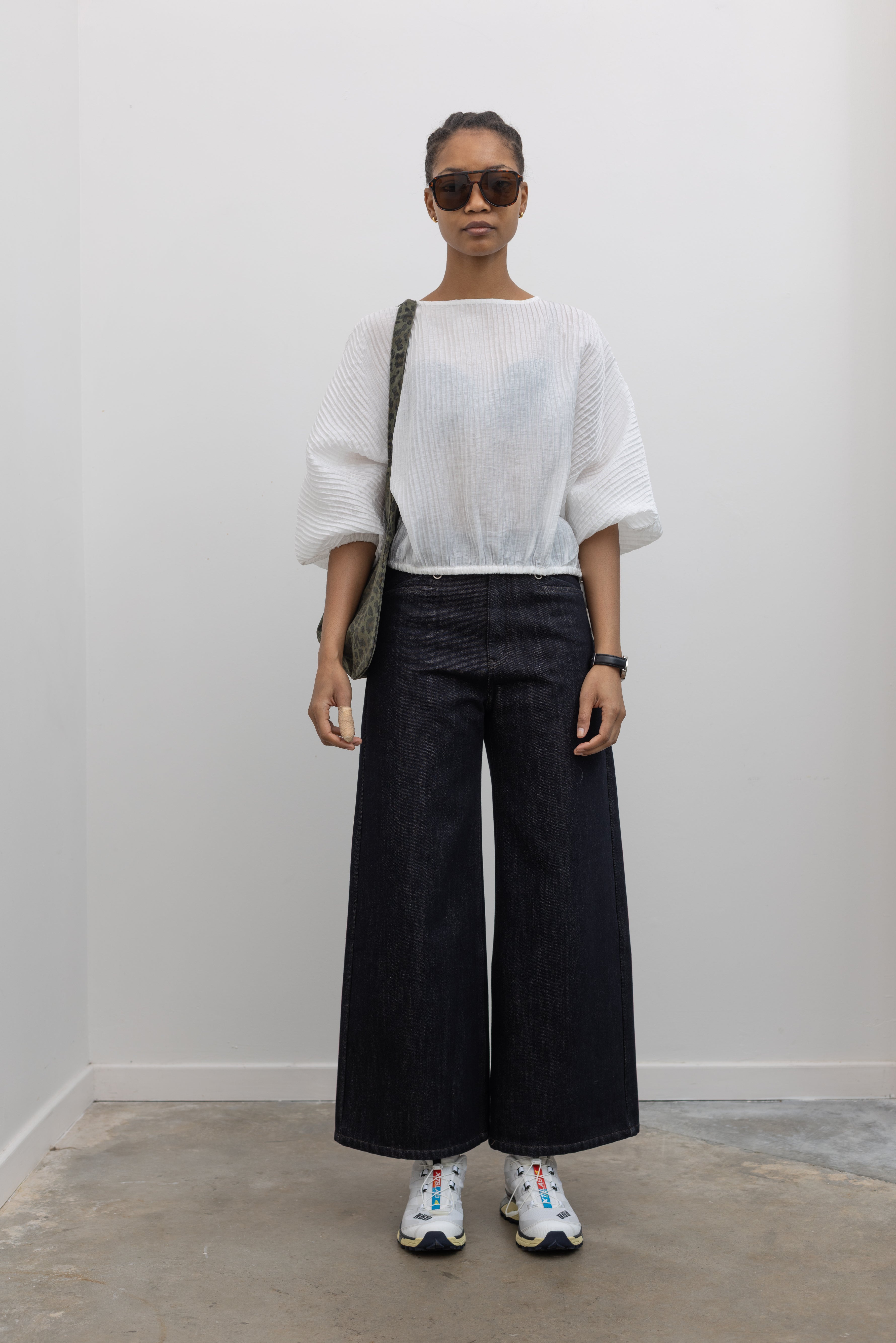 Full length view of a woman standing wearing Collective brand dark wash fleece lined wide-leg, high-rise jeans with squared off pockets with silver hardware and a white top at Alas Eius.