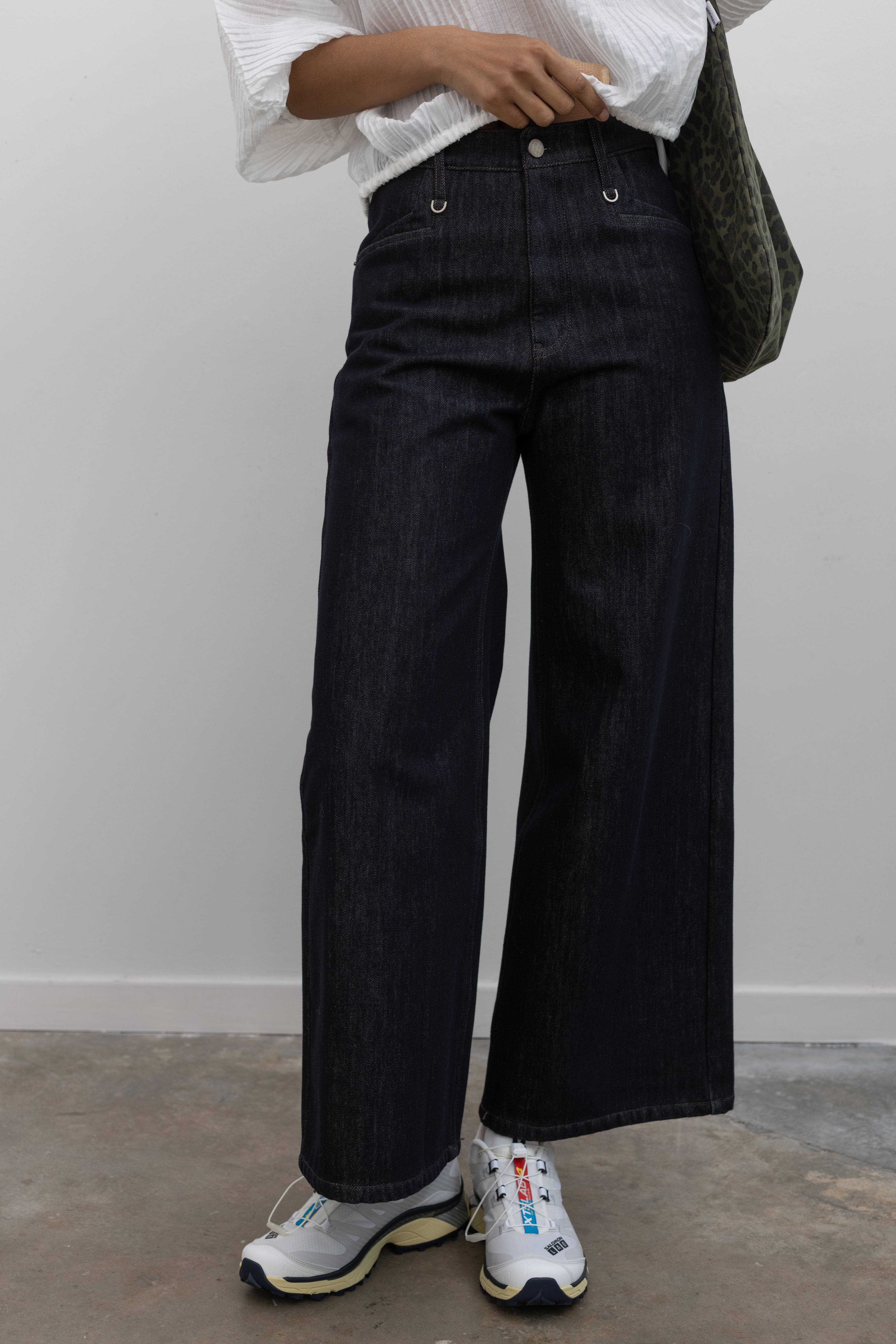 Woman wearing Collective brand dark wash fleece lined wide-leg, high-rise jeans with squared off pockets with silver hardware paired with Salomon sneakers at Alas Eius.