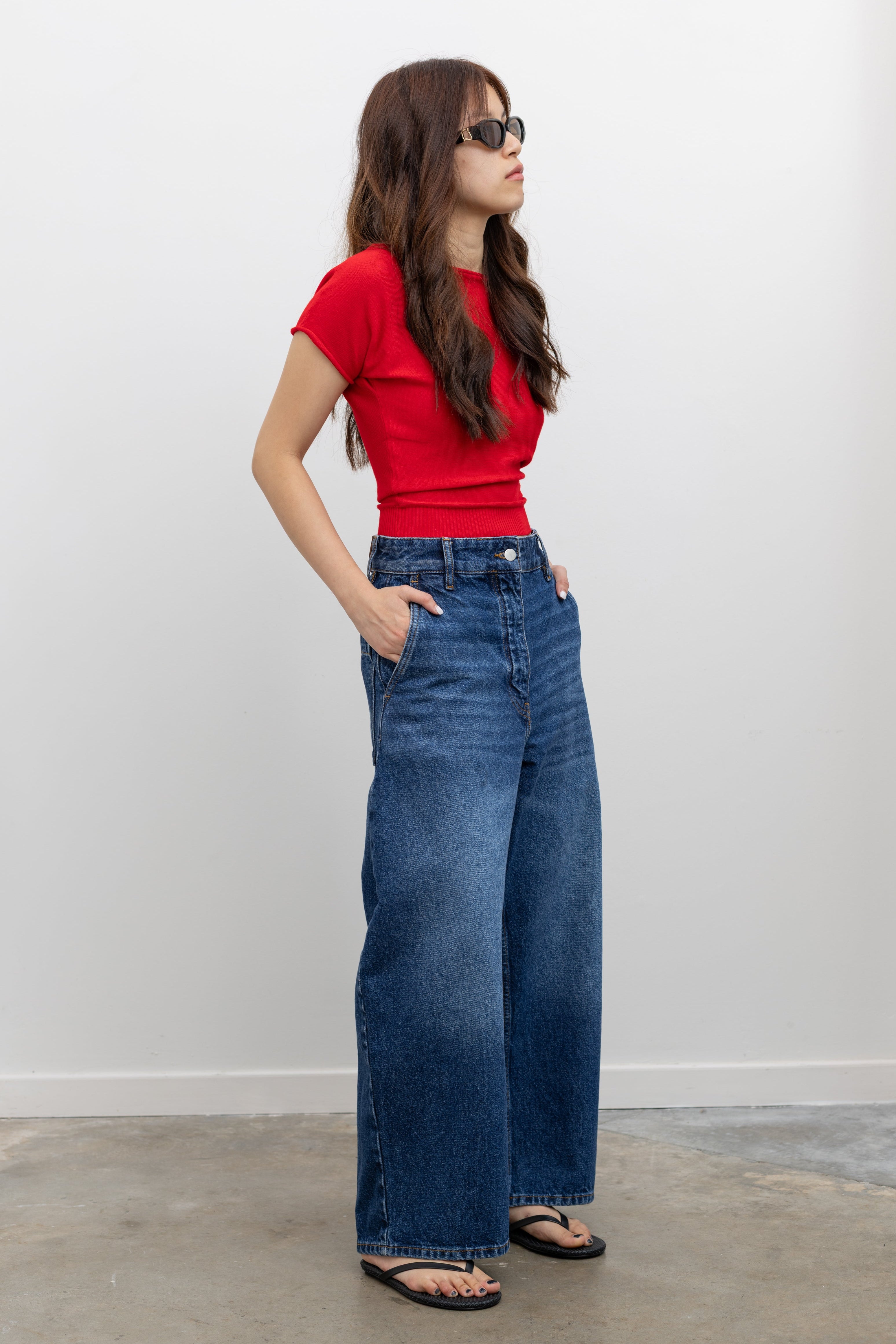 Woman wearing an elevated basic top in a Collective red knit short sleeve fitted cropped tee with Studio Nicholson wide crop denim jeans at Alas Eius. 