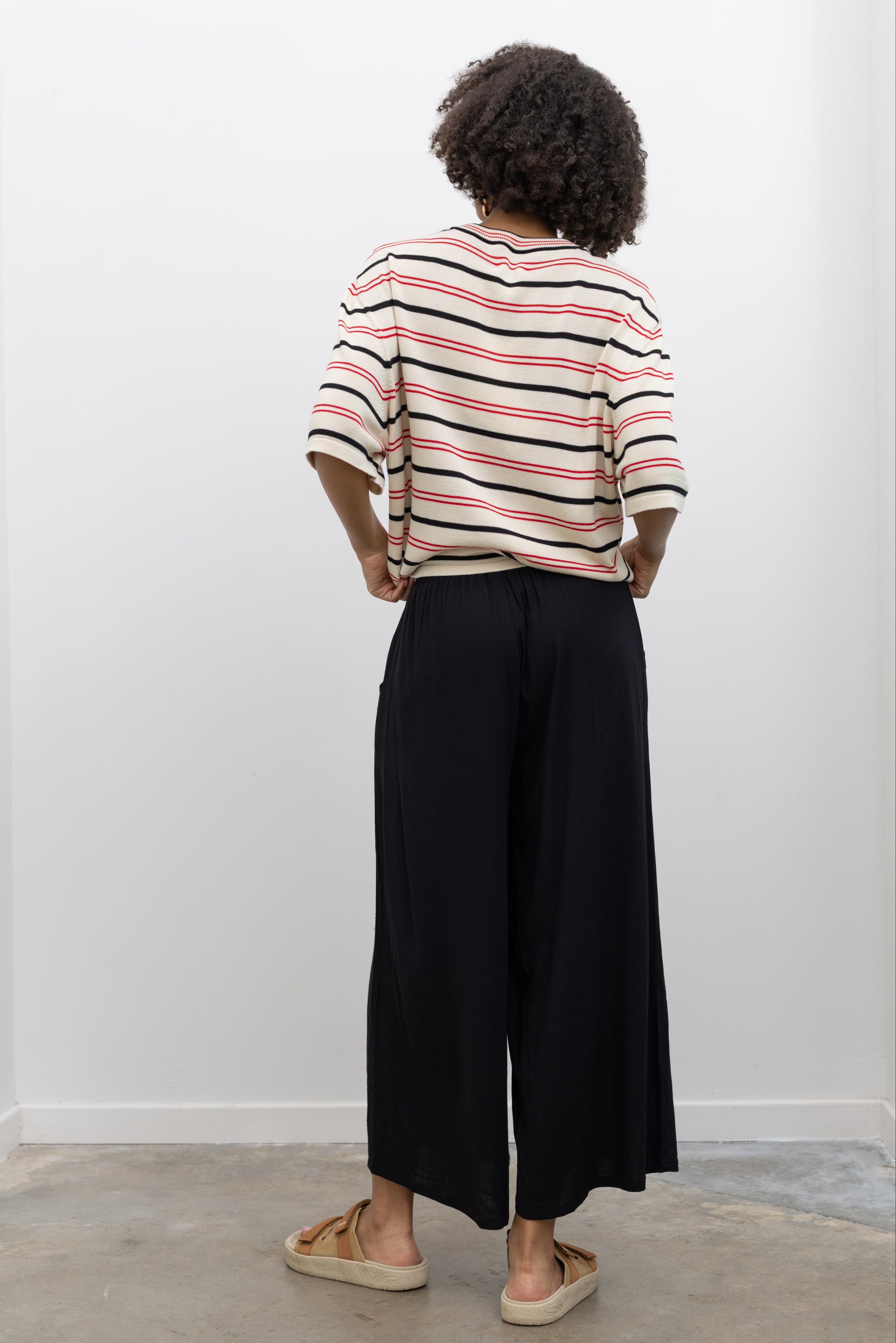 Woman wearing chic summer fashion in Collective black elastic waistband flowy pull on cropped pants with a Cordera organic cotton striped t-shirt and Veja tan suede slide sandals at Alas Eius. 