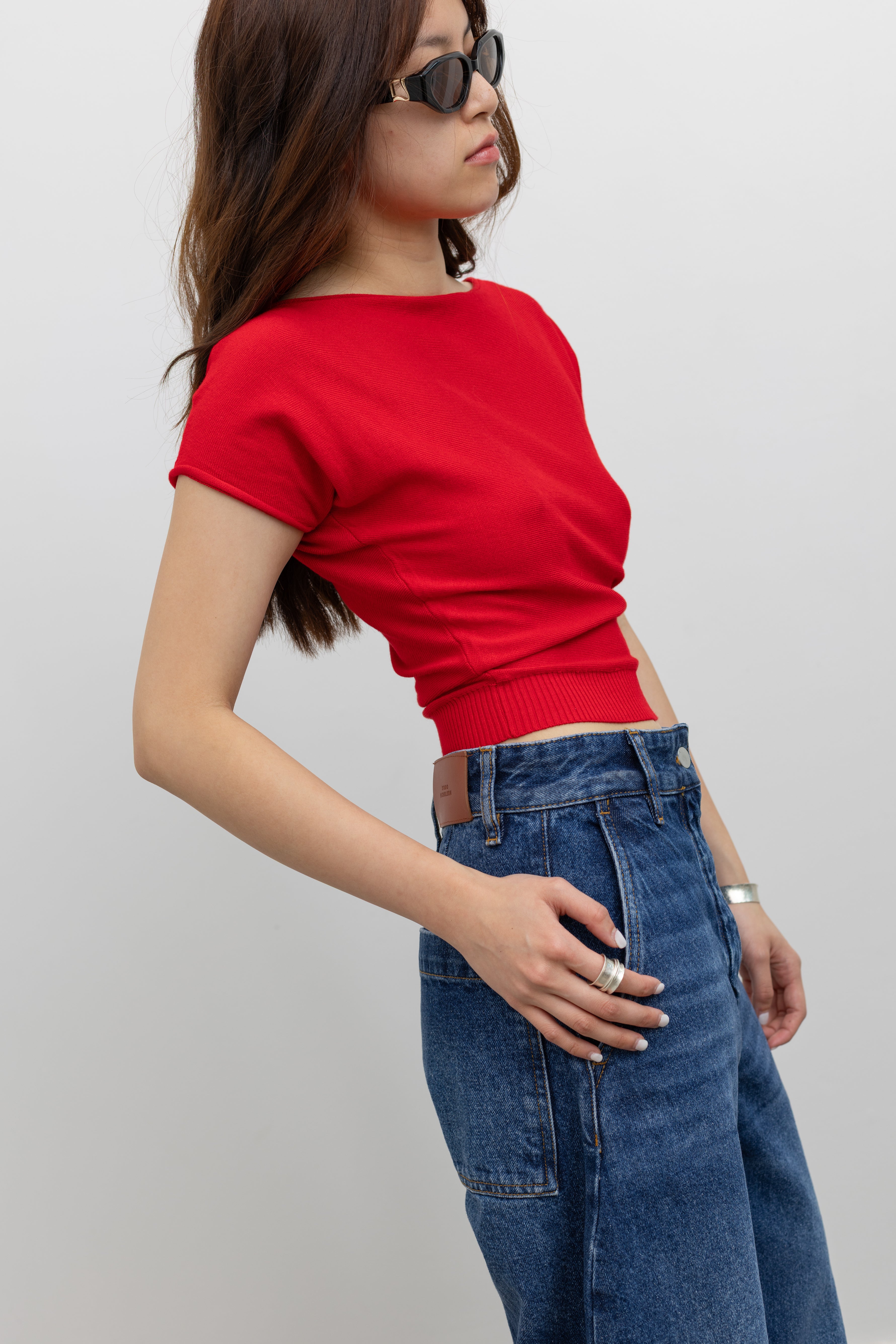 Side view of a woman wearing summer weekend outfit in a Collective red knit short sleeve fitted crop top with Studio Nicholson wide crop denim jeans at Alas Eius. 
