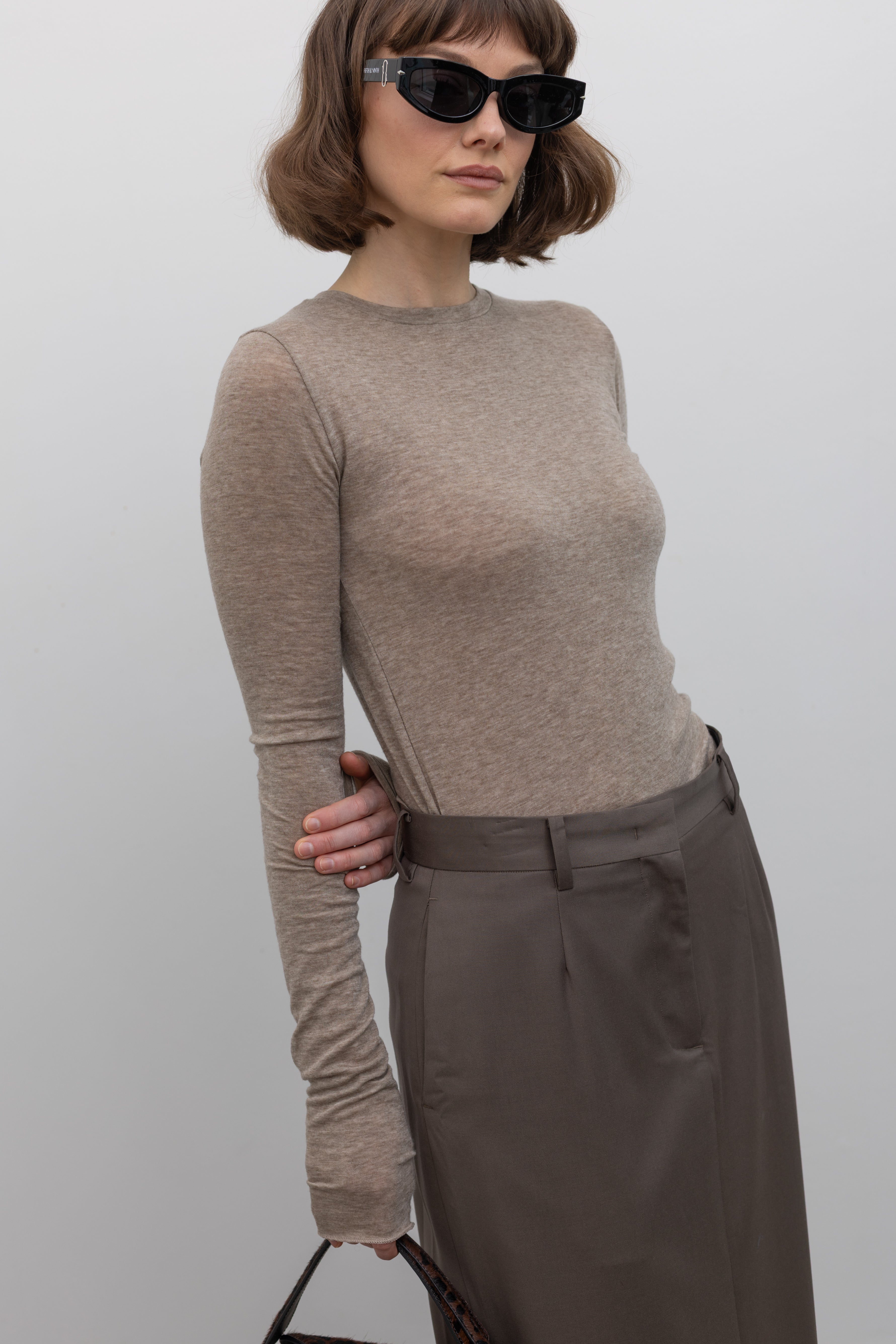 3/4 view of a woman wearing an elevated capsule wardrobe essential in a Collective Brand Beige Merino Wool Long Sleeve Fitted Top paired with a class tailored pencil skirt at Alas Eius. 