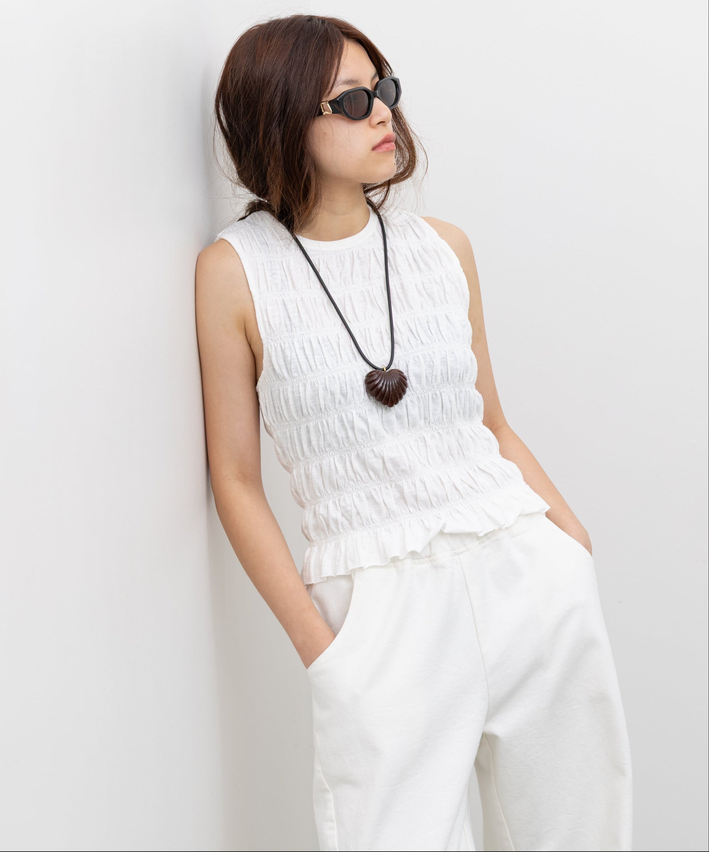 Collective Sleeveless smocked cotton top with body-sculpting fit, high neck, and ruffle hem paired with a Rachel Comey Minimal Shell Heart Pendant Necklace at Alas Eius