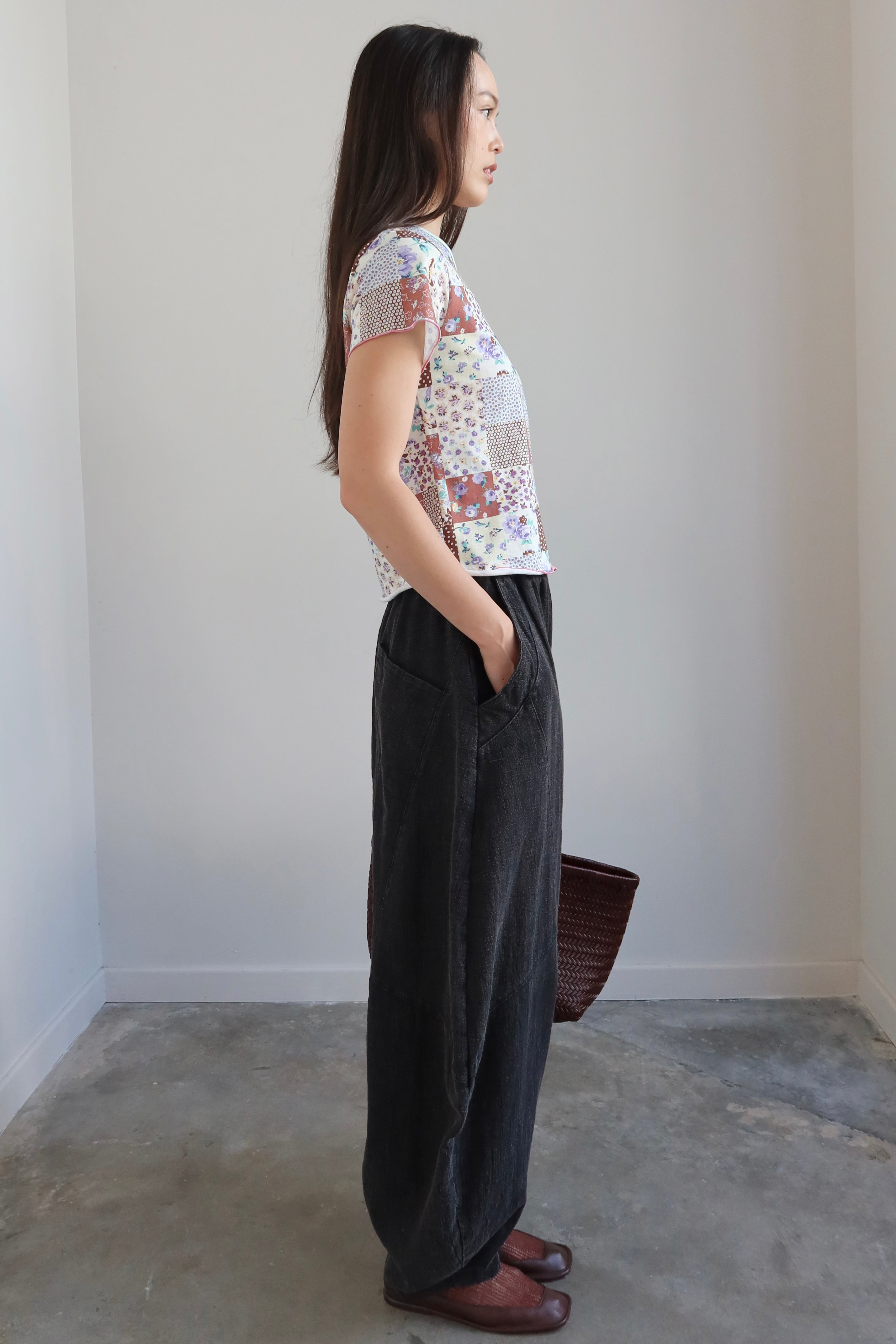 Full length side view of a Woman wearing a Collective Quilted Pattern Floral Tee Shirt  with oversized parachute pants at Alas Eius