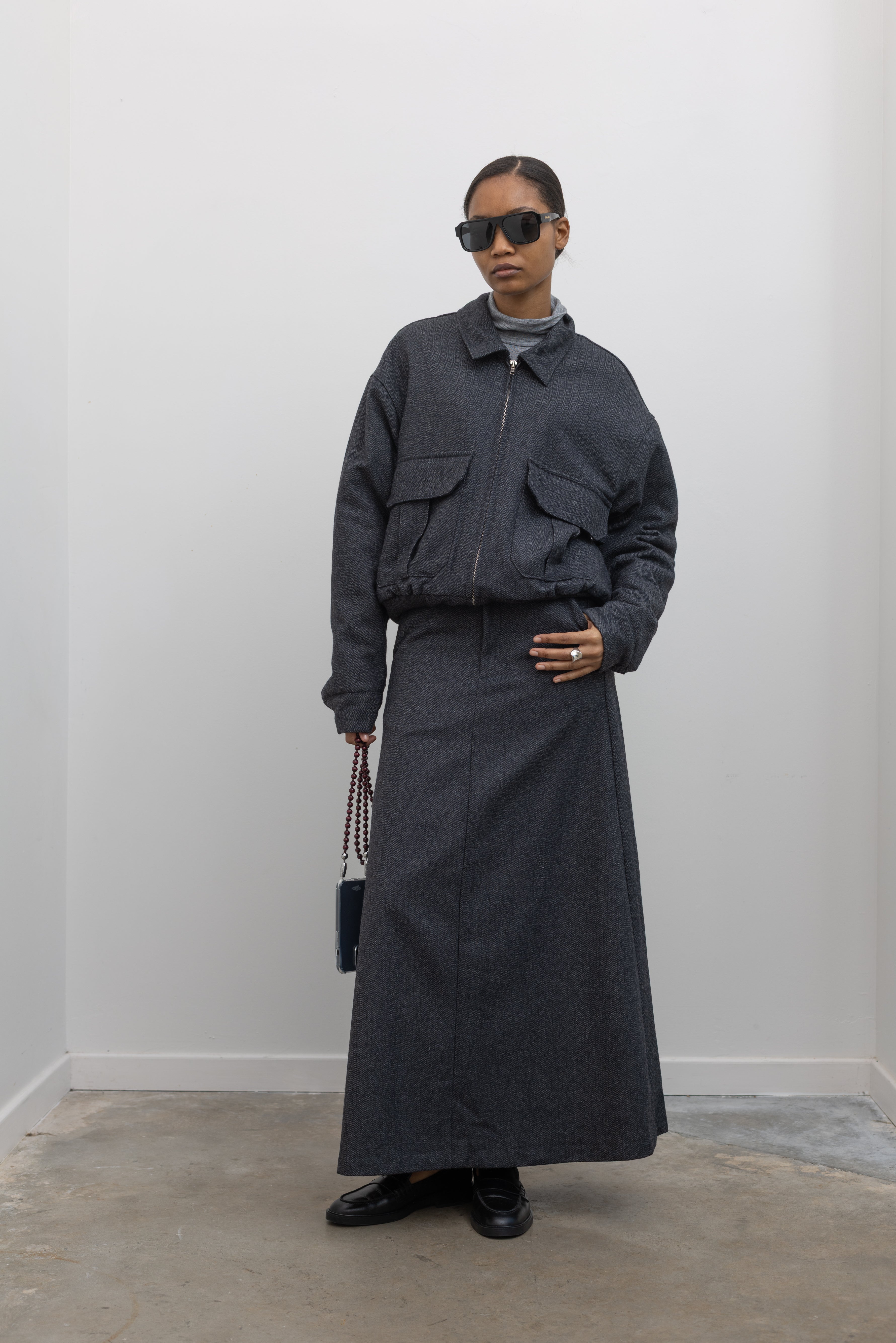 Full length front view of a Collective Charcoal Wool Blend Herringbone Collared Quilted Zip Bomber Jacket paired with a Collective A-line tailored gray wool blend herringbone maxi skirt at Alas Eius.