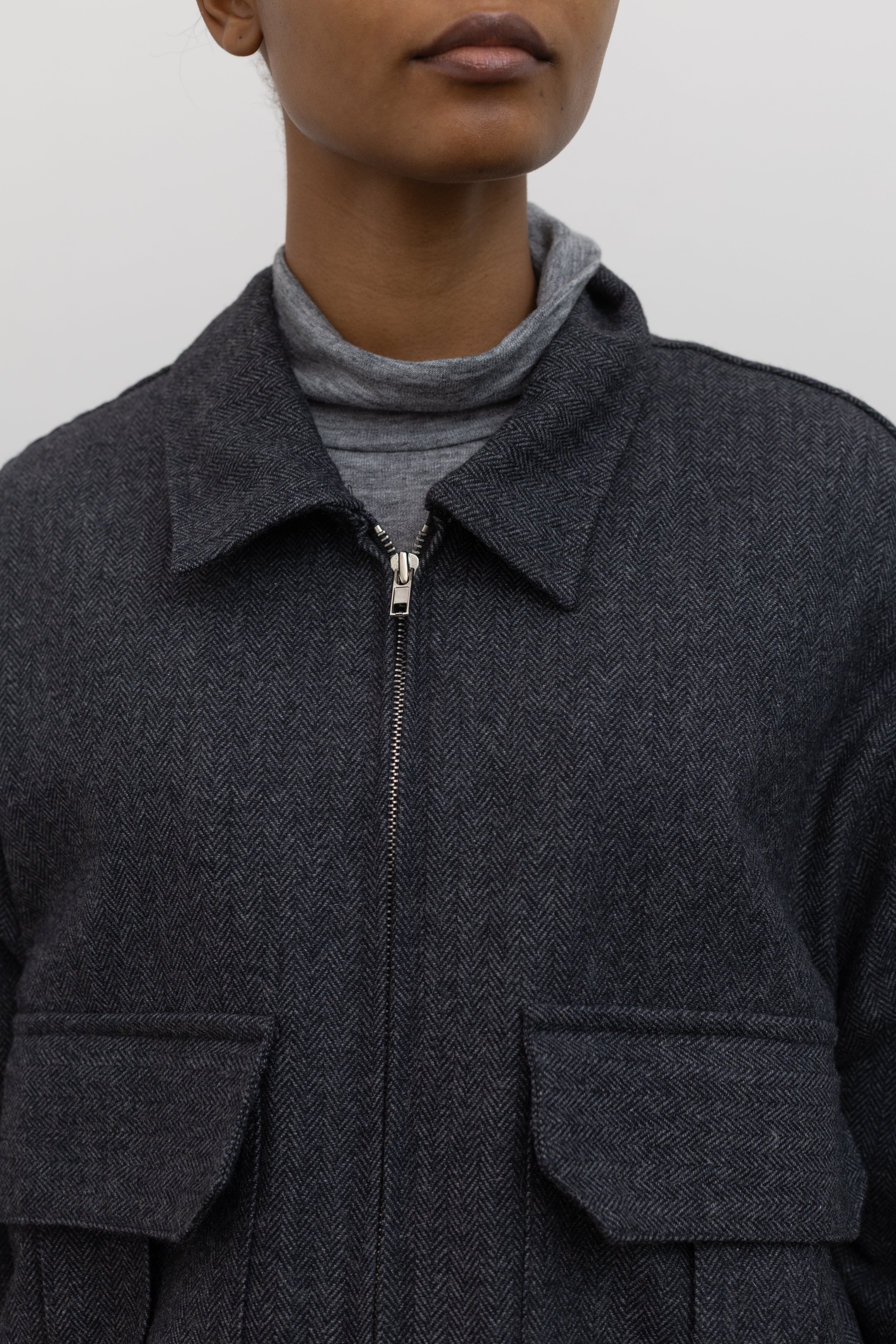 Close-up front view of a Collective Charcoal Wool Blend Herringbone Collared Quilted Bomber Jacket paired with a Collective A-line tailored gray wool blend herringbone maxi skirt at Alas Eius.