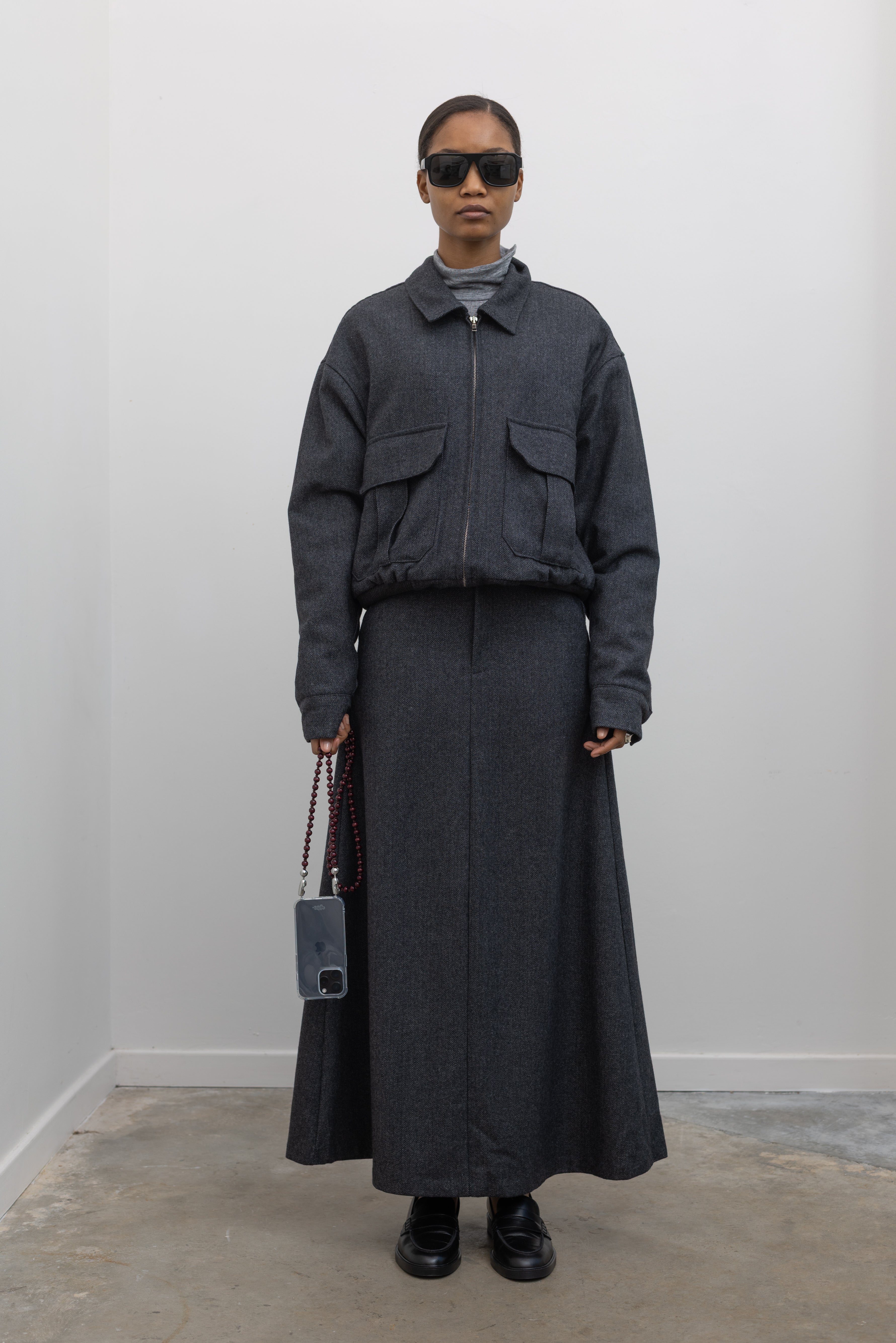 Full length front view of a Collective Charcoal Wool Blend Herringbone Collared Quilted Bomber Jacket paired with a Collective A-line tailored gray wool blend herringbone maxi skirt at Alas Eius.