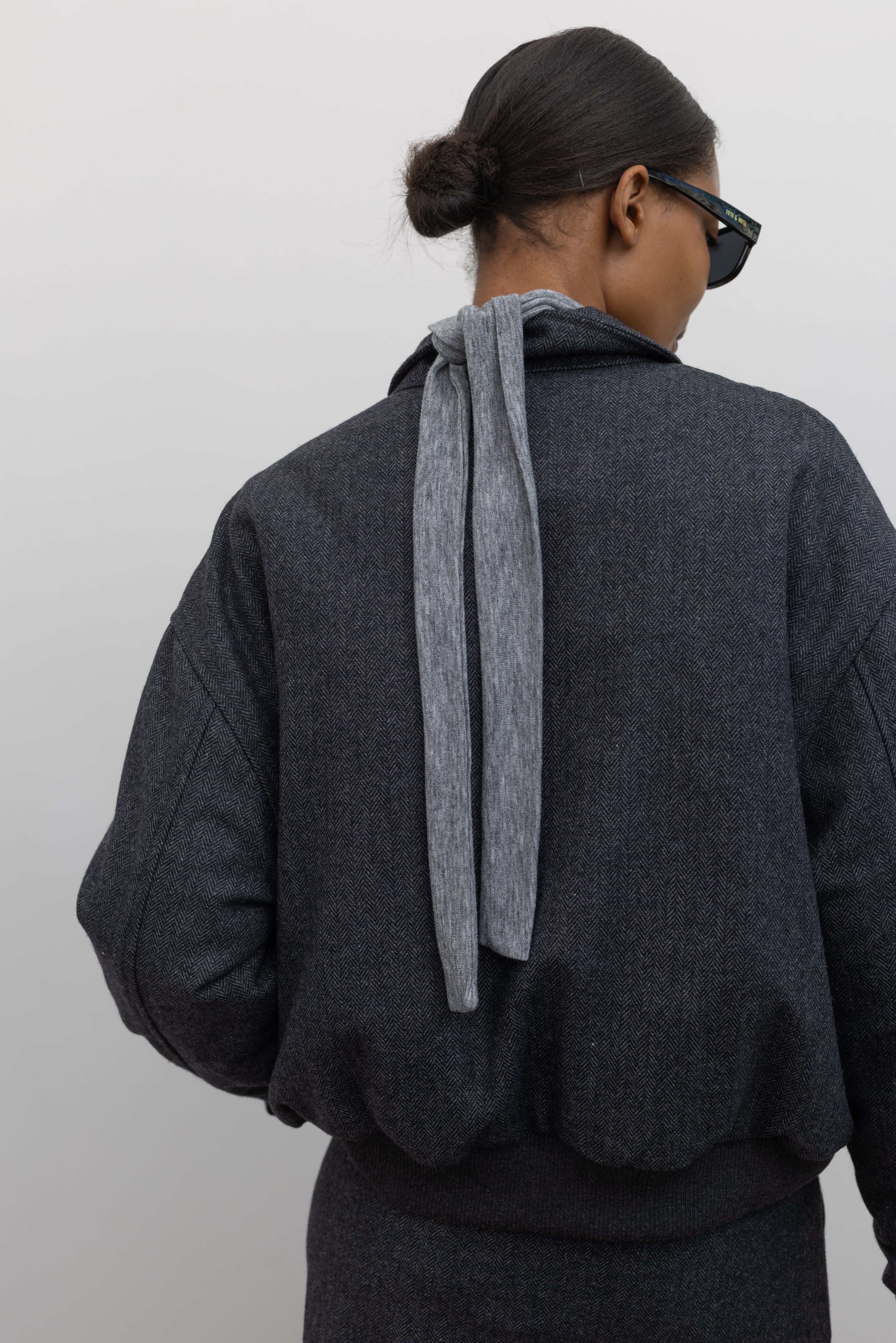 Full length back view of a Collective Charcoal Wool Blend Herringbone Collared Quilted Bomber Jacket paired with a Collective A-line tailored gray wool blend herringbone maxi skirt at Alas Eius.