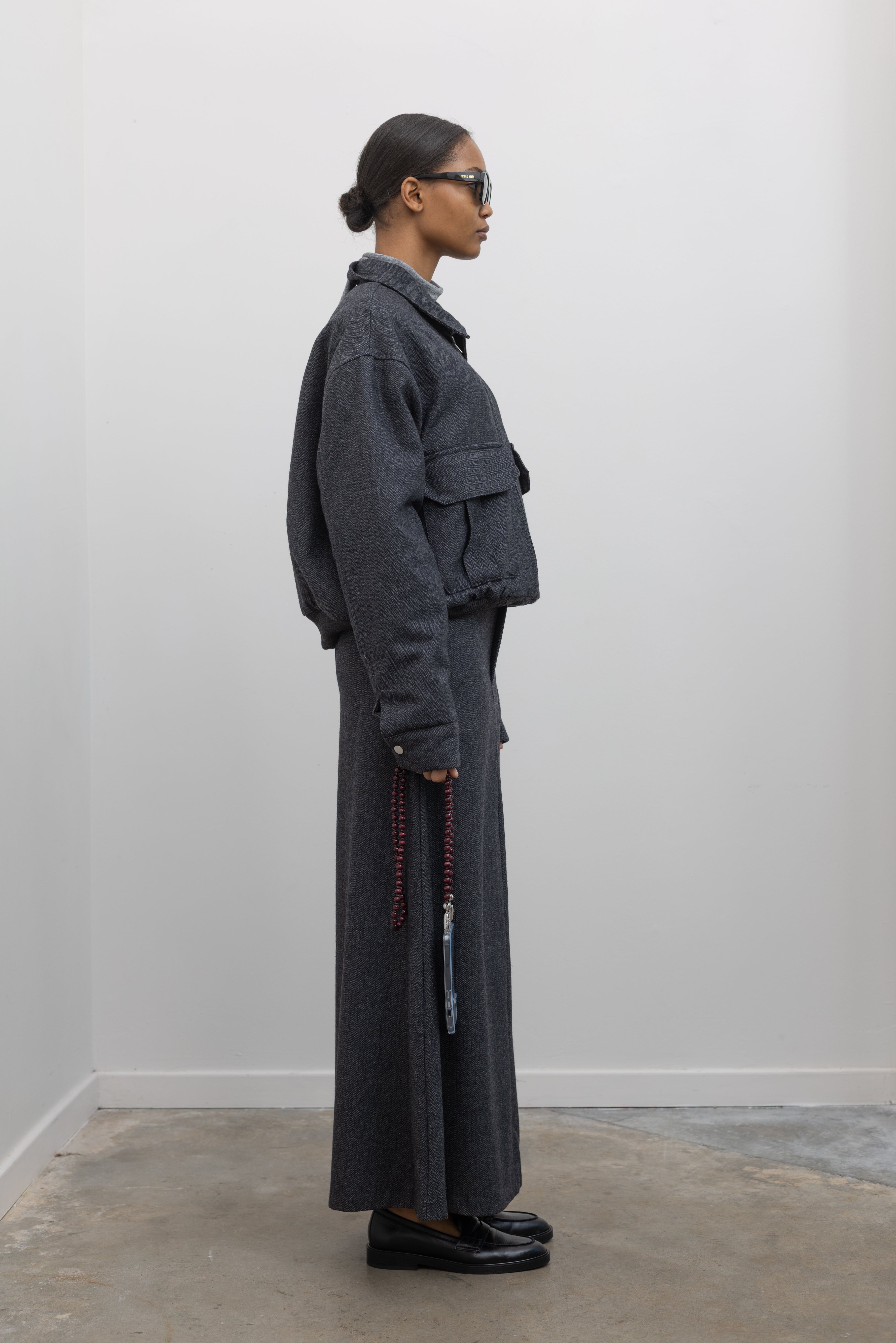 Full length side view of a Collective Charcoal Wool Blend Herringbone Collared Quilted Bomber Jacket paired with a Collective A-line tailored gray wool blend herringbone maxi skirt at Alas Eius.