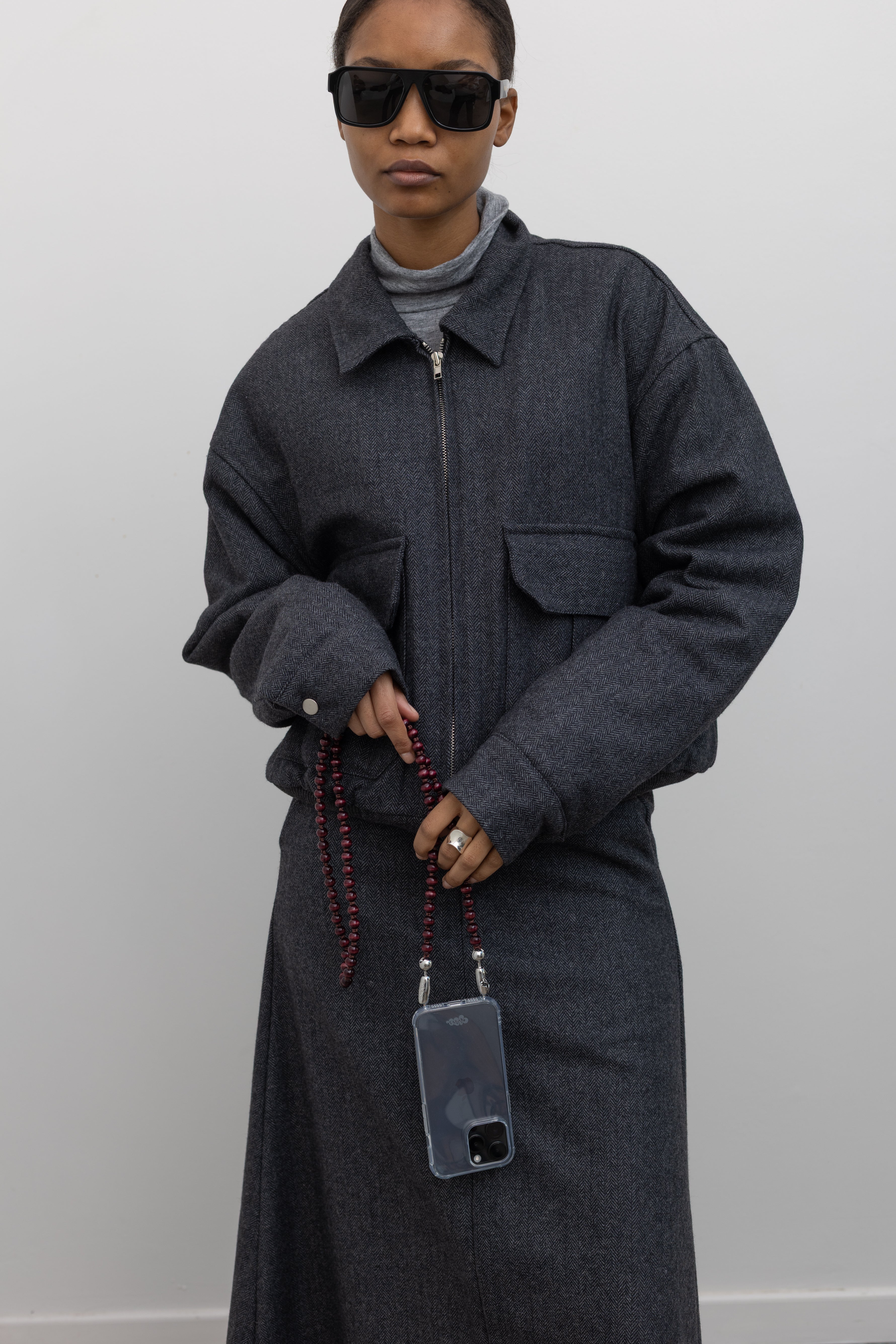 Close-up front view of a Collective Charcoal Wool Blend Herringbone Collared Quilted Bomber Jacket paired with a Collective A-line tailored gray wool blend herringbone maxi skirt at Alas Eius.