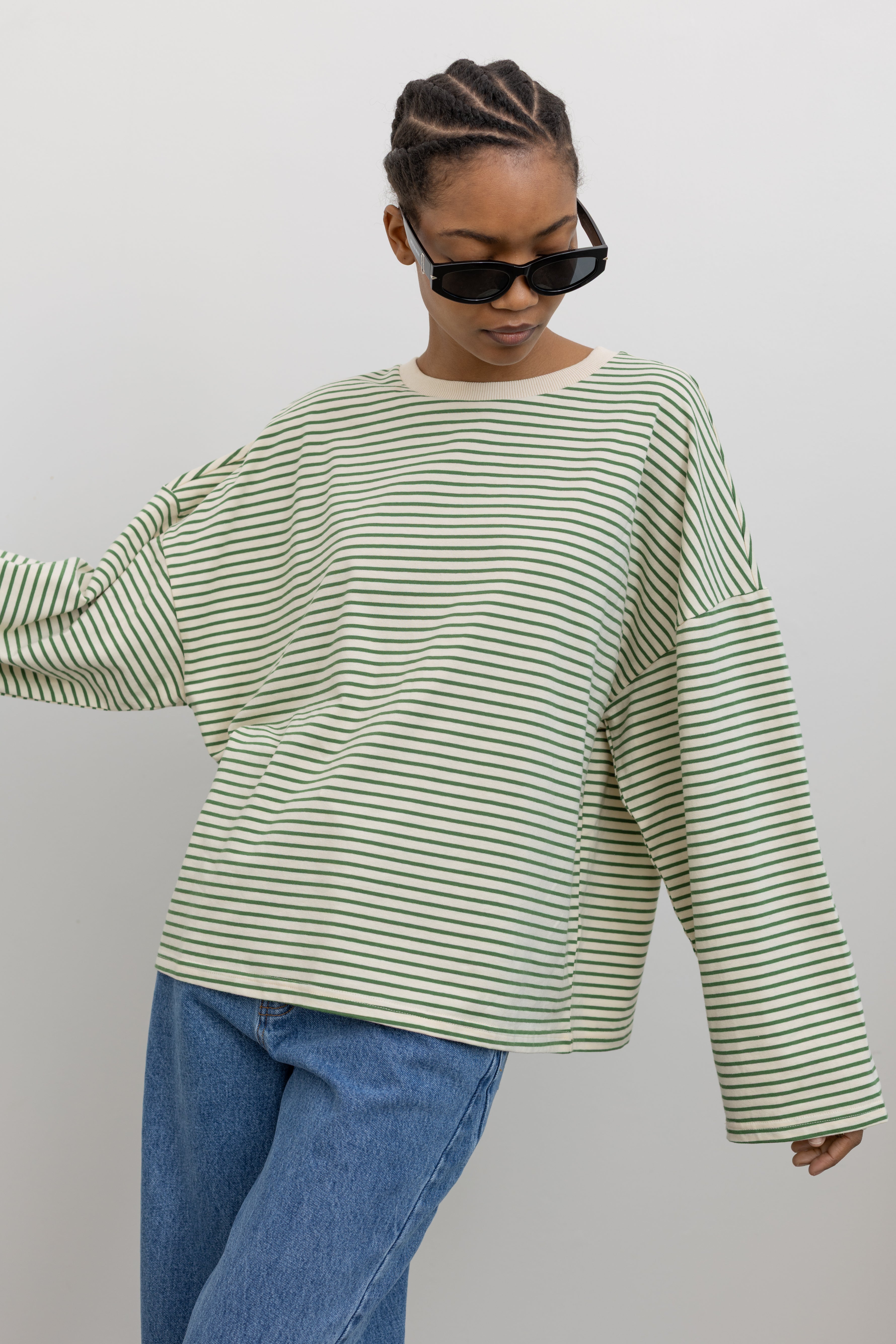 Woman in motion wearing wearing Spring casual fashion in a Collective green and natural stripe dropped shoulder long sleeve cotton  oversized top paired with light wash denim at Alas Eius.