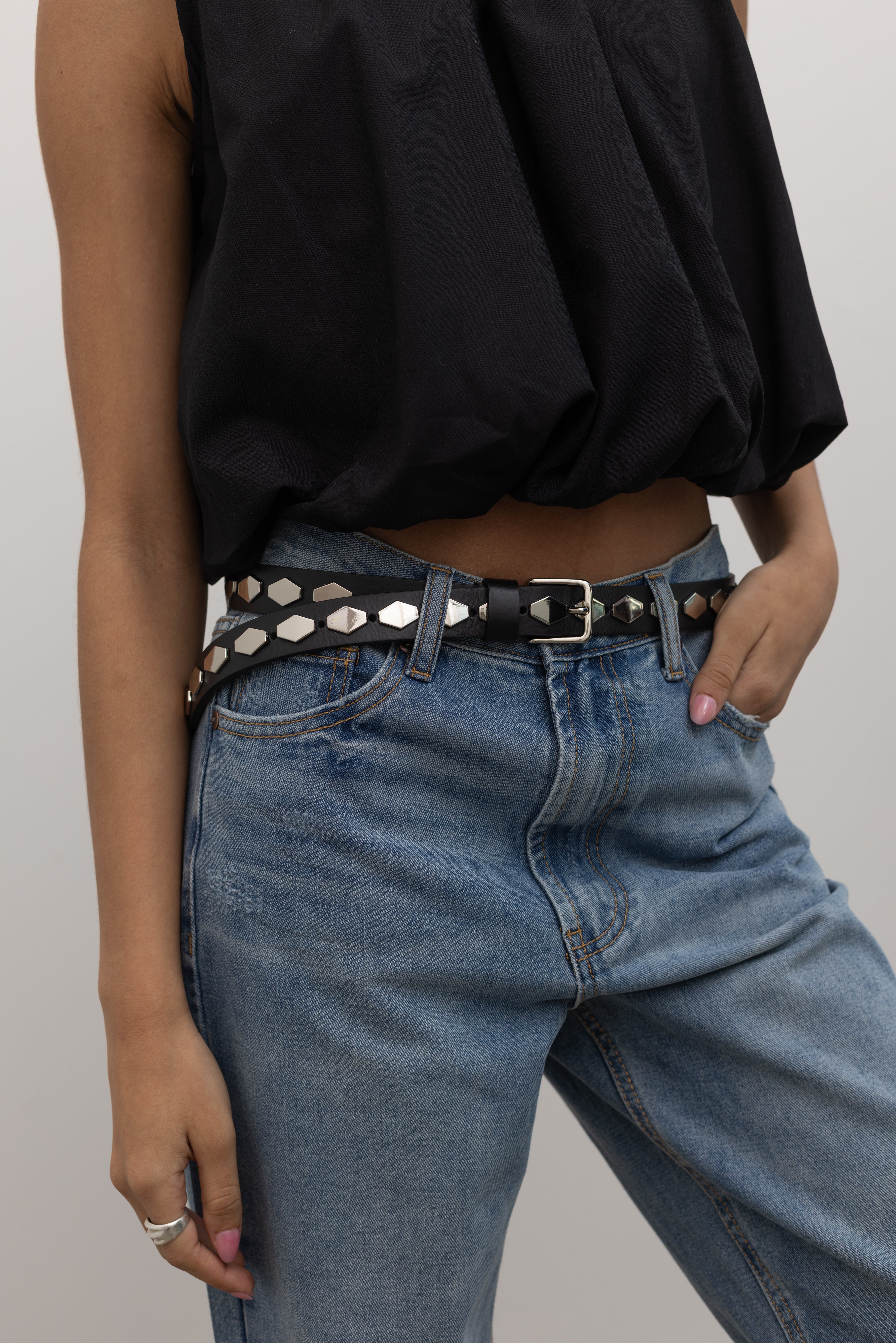Woman wearing an elevated classic essential accessory in a Collective brand Italian black leather belt with shiny silver honeycomb shaped hardware paired with light wash denim jeans and a black balloon hem top at Alas Eius. 