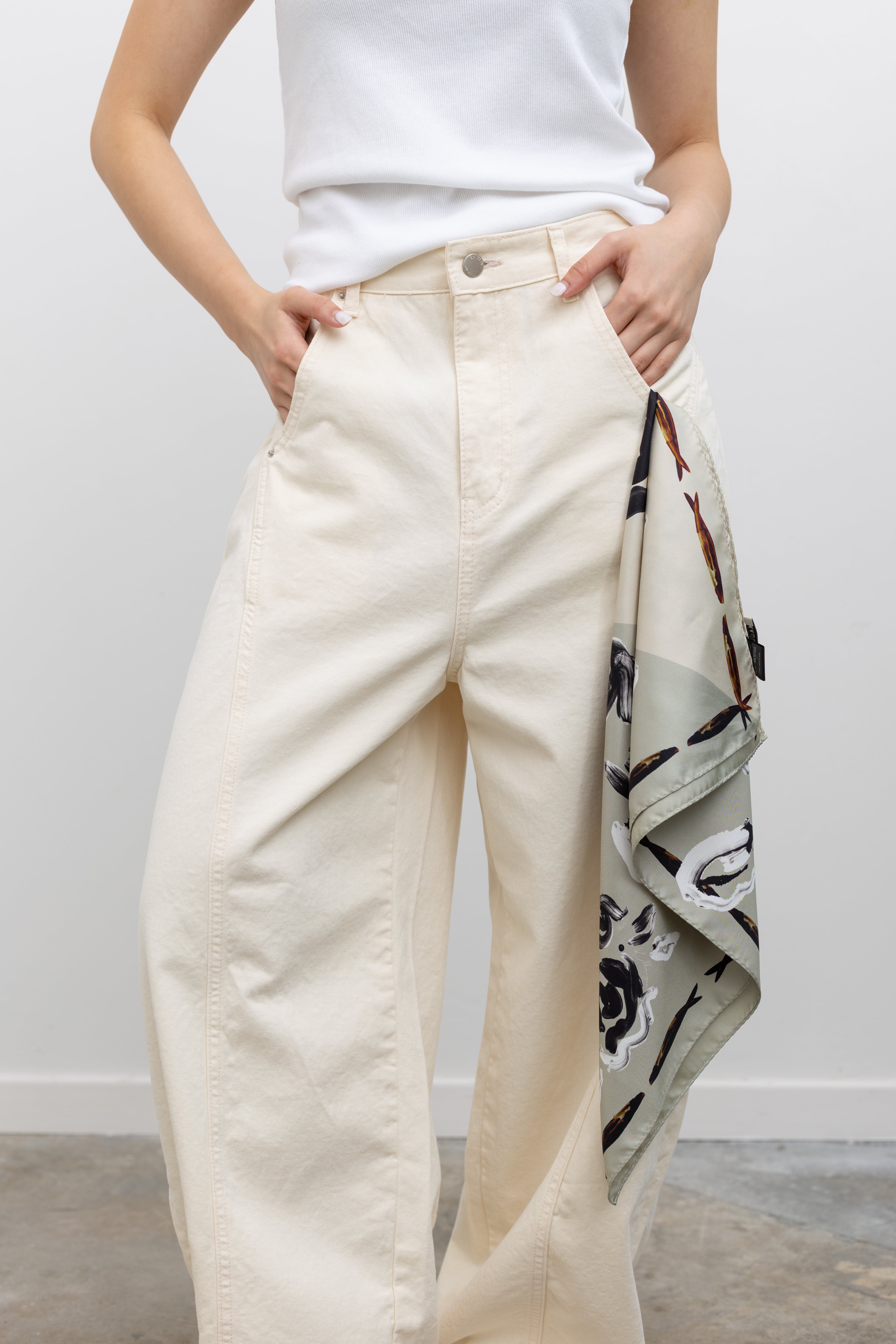 Model wearing elevated summer fashion in Collective ivory heavy-weight cotton denim jeans with a structured wide-leg silhouette, curved paneling, and relaxed oversized fit paired with an Alas Eius label logo tank and Veja slide sandals at Alas Eius.