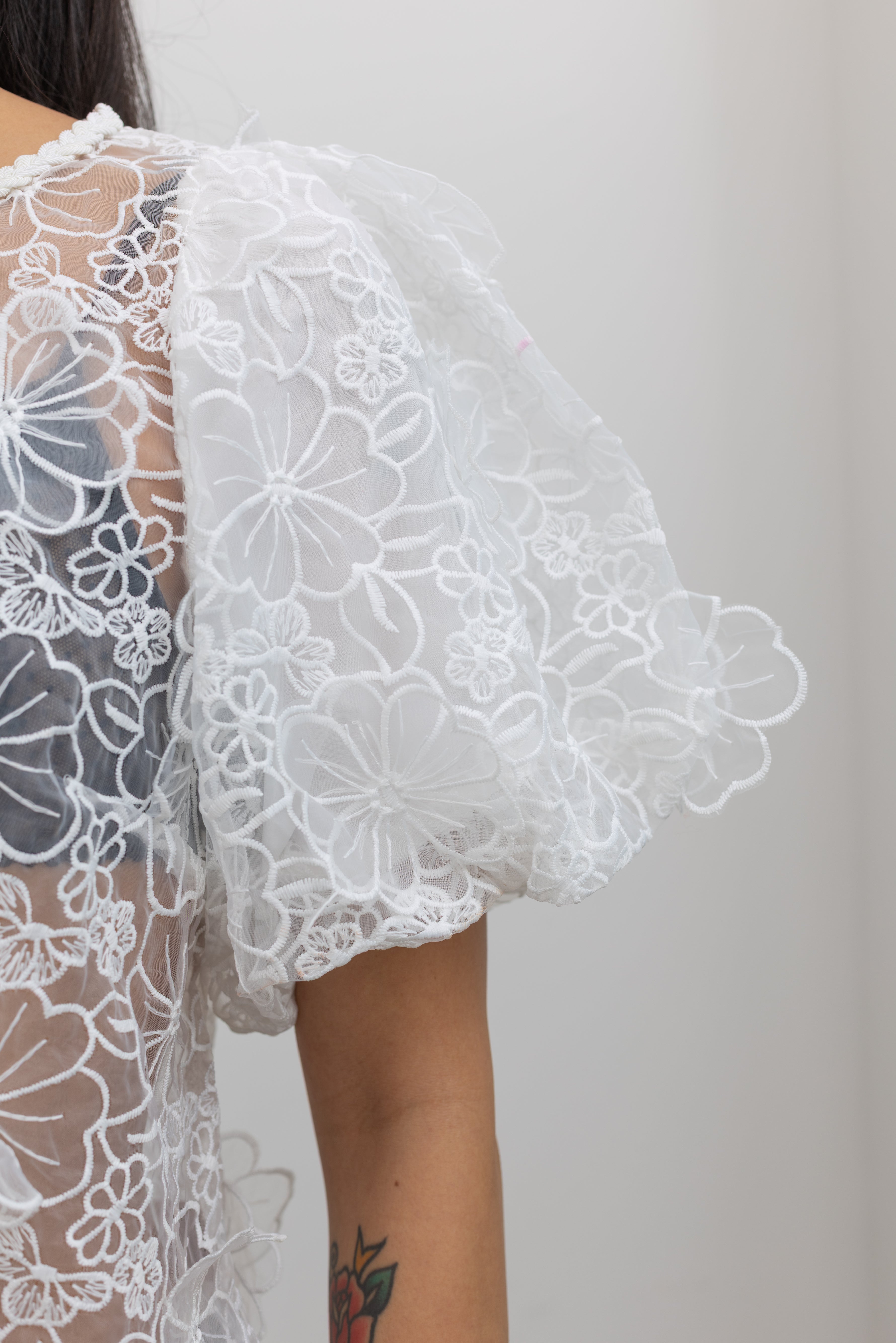 Close-up detailed view of Collective brand ivory floral embroidered organza billow sleeve statement top at Alas Eius. 