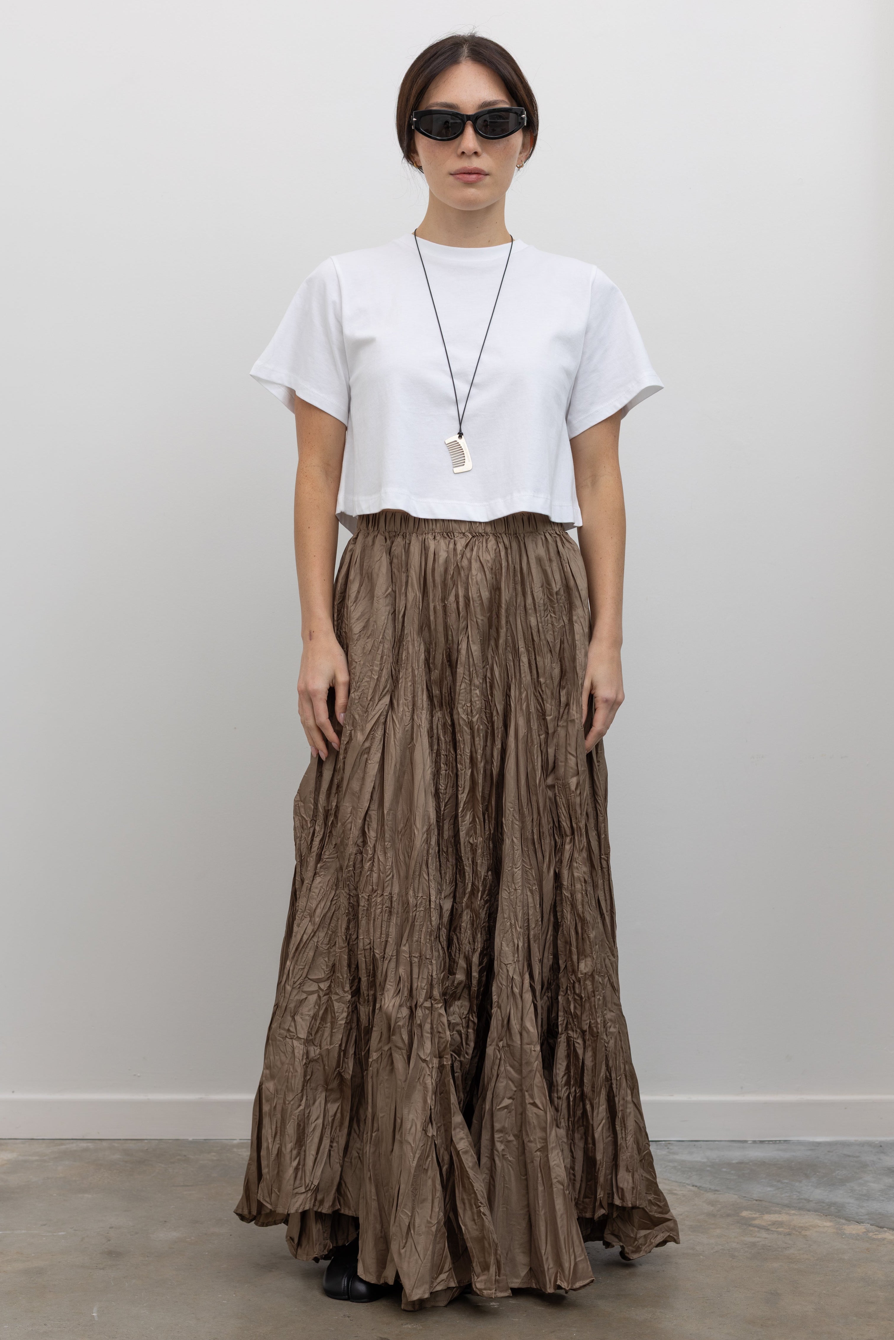 Full length front view of a woman wearing contemporary spring fashion in an Alas Eius label cropped white t-shirt paired with a Collective Khaki Crinkle Textured Maxi Skirt at Alas Eius. 