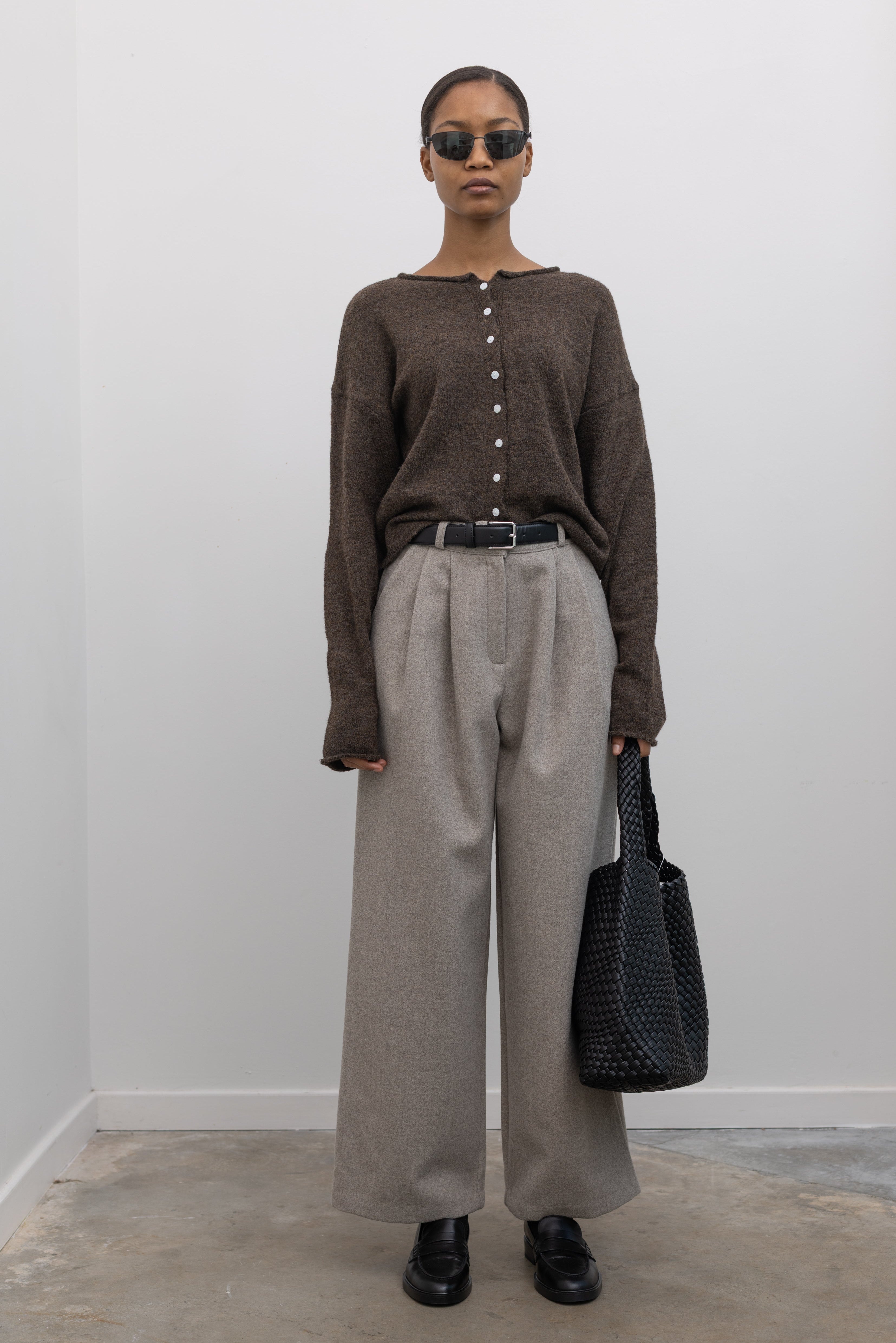 Full length front view of a woman standing wearing sophisticated capsule wardrobe staple in a Collective label Beige Tailored Wool Blend Wide Leg, high rise Pants paired with a button front sweater and black leather loafers at Alas Eius. 