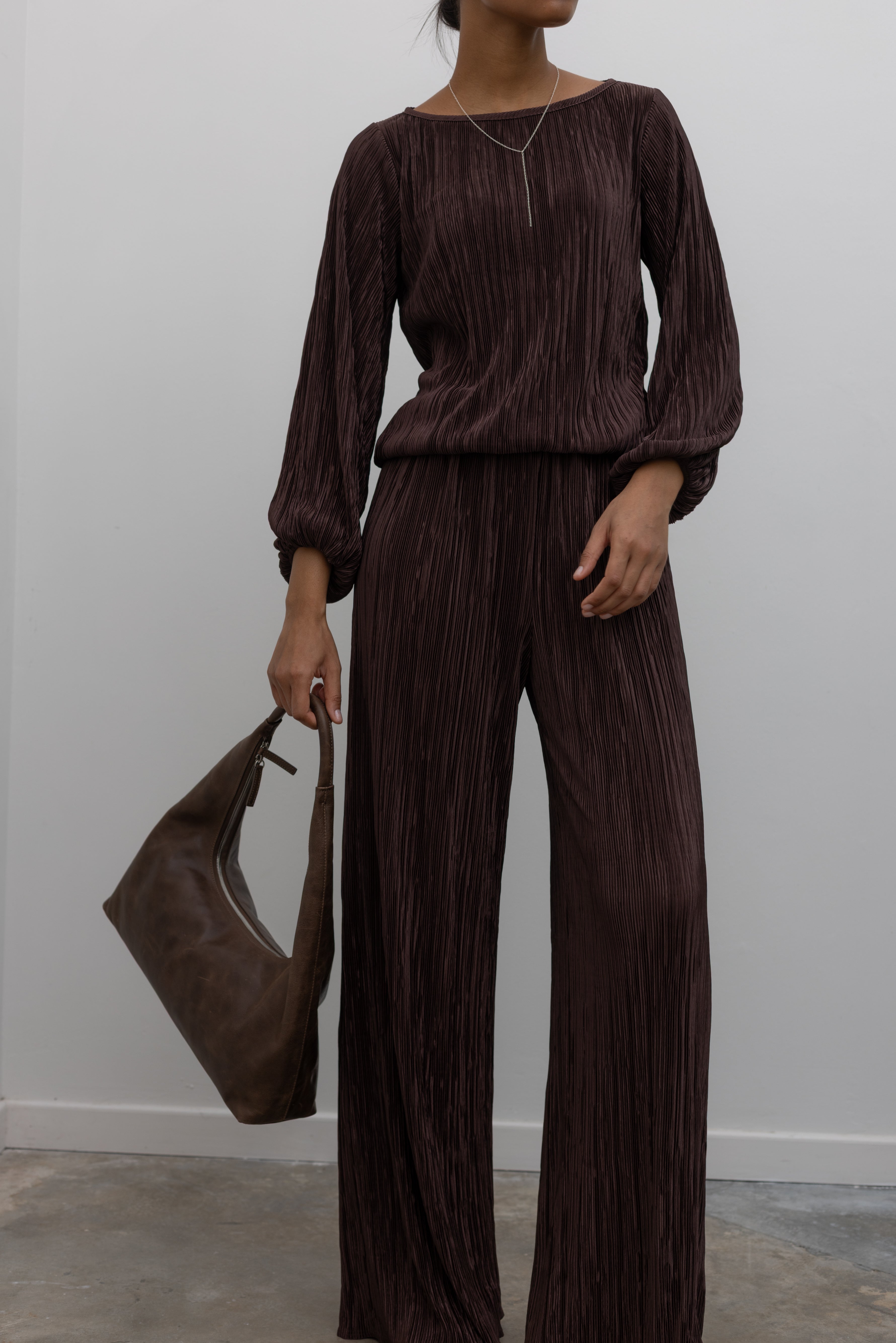 Woman wearing a sophisticated chocolate brown plisse long sleeve top with its coordinating pants creating the perfect elevated or casual outfit. 