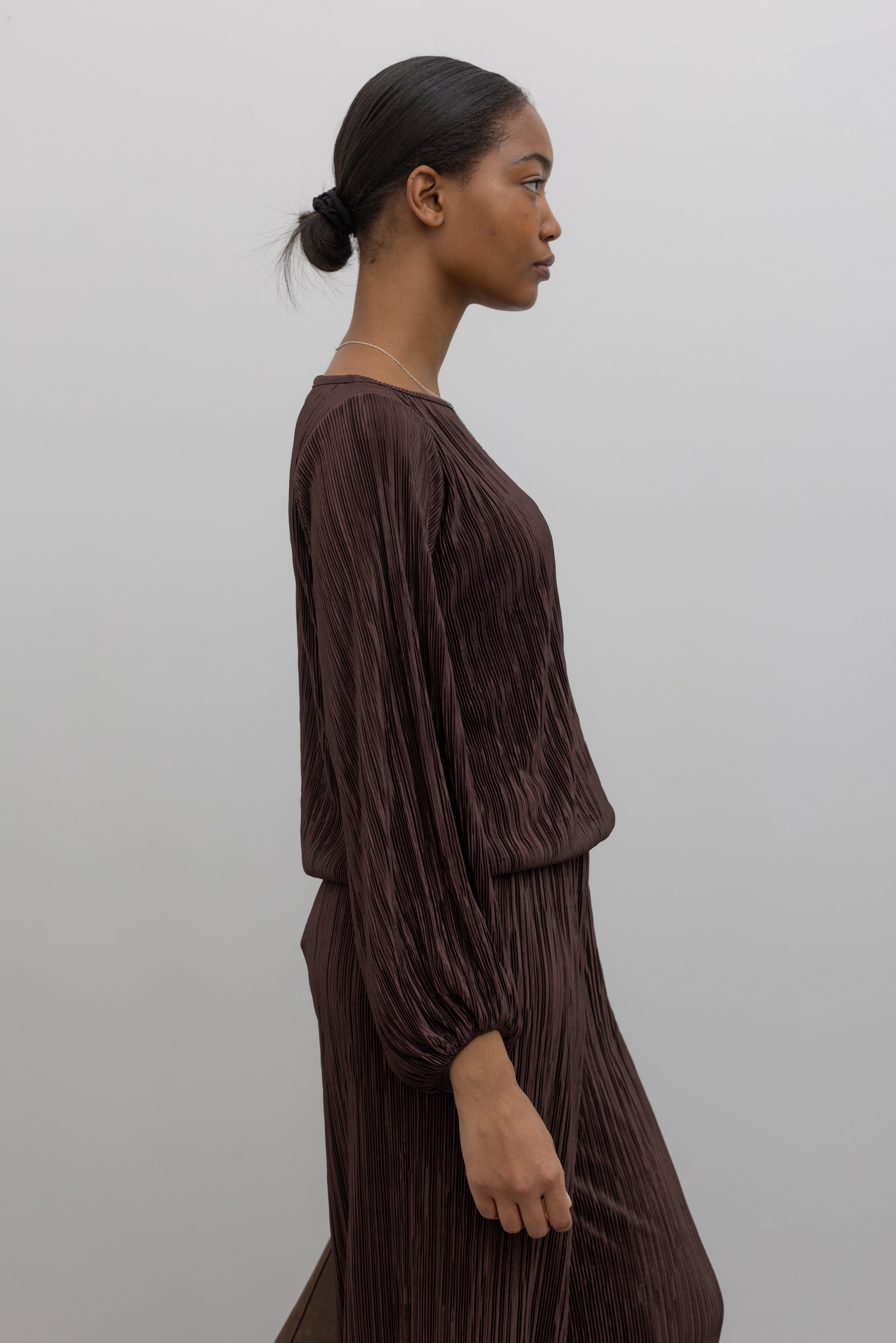 Side view of a woman wearing a sophisticated chocolate brown plisse long sleeve top with its coordinating pants creating the perfect elevated casual outfit. 