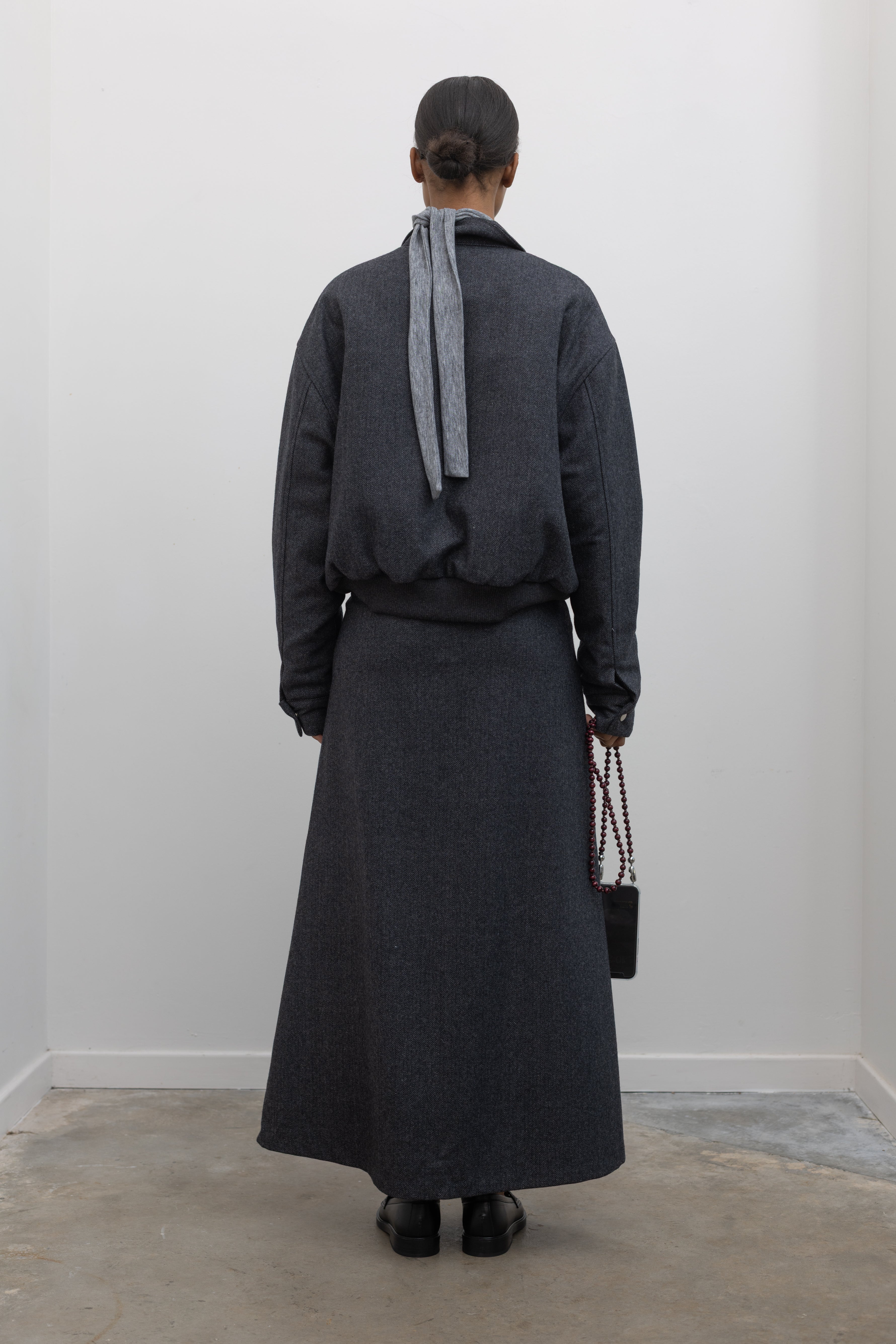 Full length back view of a Collective Charcoal Wool Blend Herringbone Collared Quilted Bomber Jacket paired with a Collective A-line tailored gray wool blend herringbone maxi skirt at Alas Eius.
