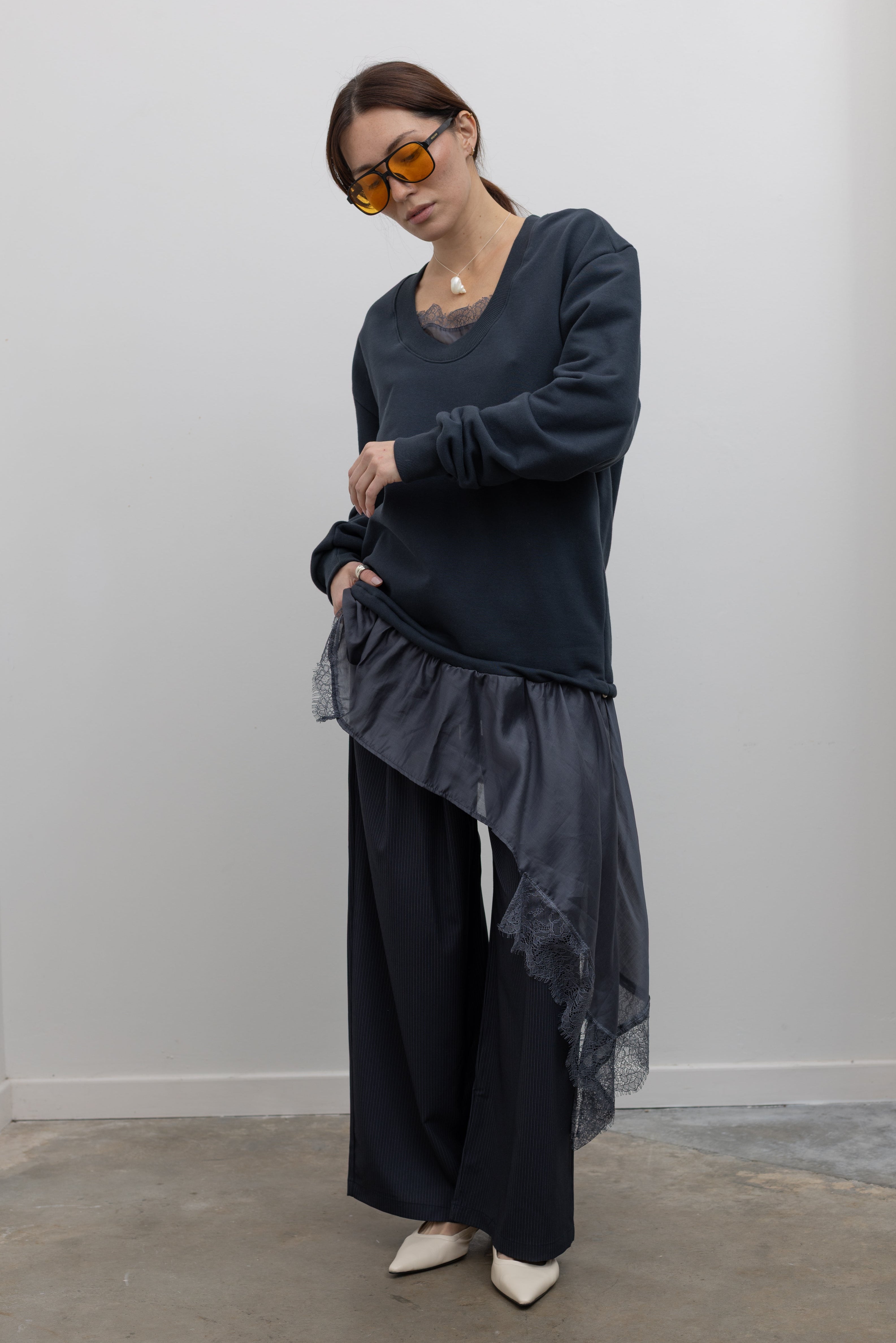 Woman standing wearing Spring fashion in a Collective Navy Lace Trim Cotton Oversized Jumper and navy blue pinstripe trousers with sunglasses and white pumps at Alas Eius 