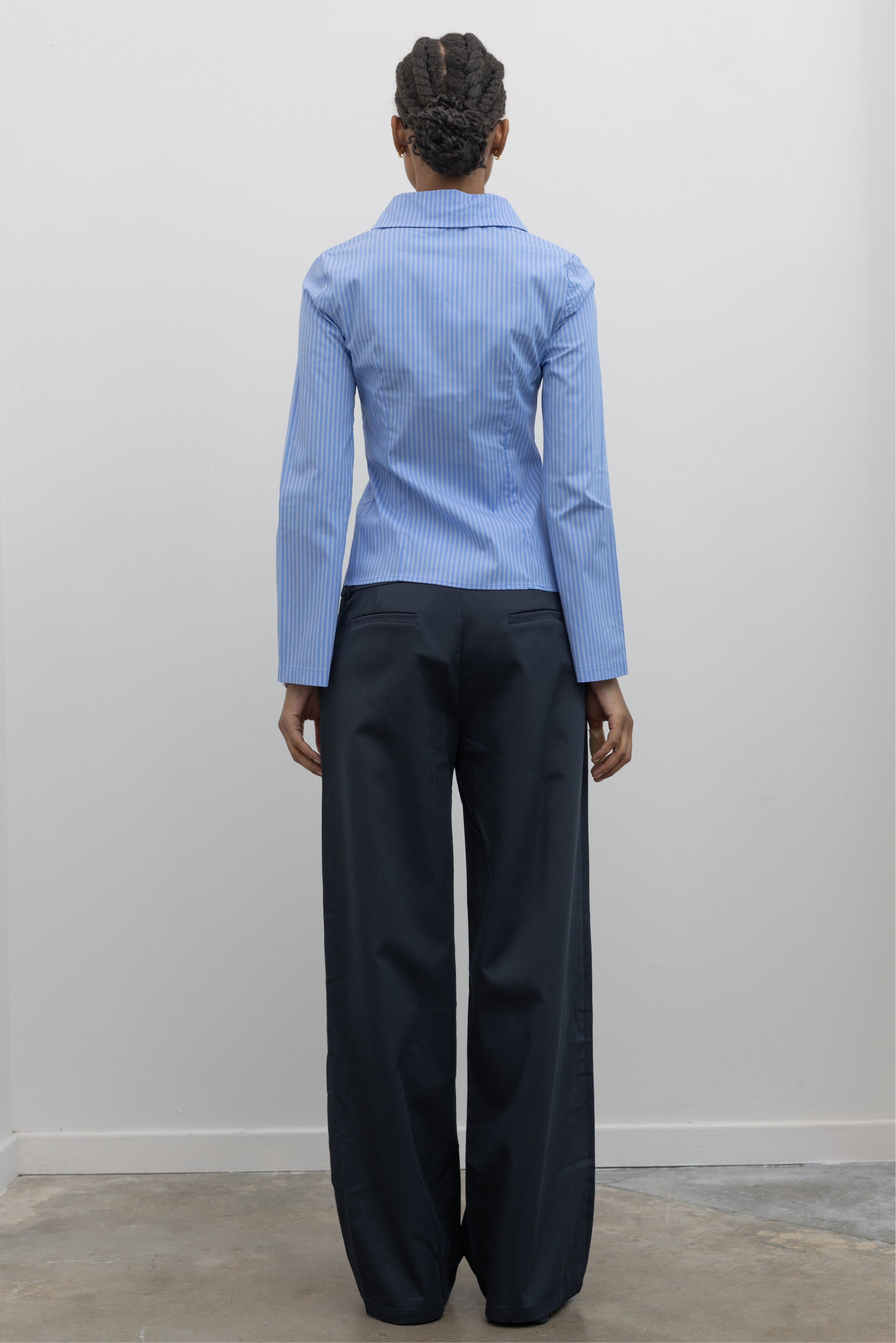 Back view of a woman in motion wearing Spring fashion in a Collective Blue Pinstripe Tailored Slim-Fit Button Down Top with flared sleeves and fabric covered buttons at Alas Eius.