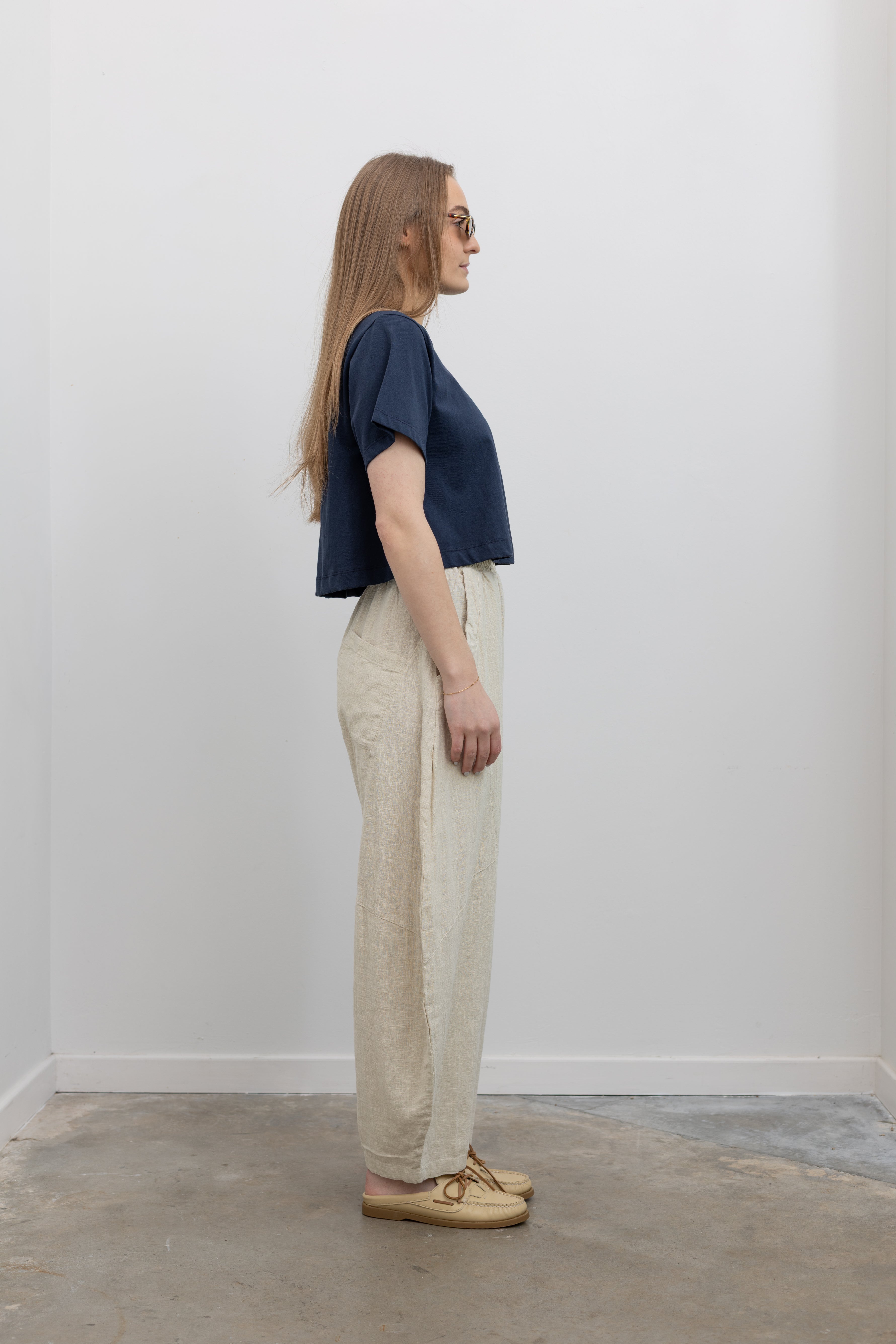 Side view of woman standing wearing Spring fashion in an Alas Eius label navy blue crop top with a pair of Collective Linen Barrel Cotton Blend Pants and leather mule shoes at Alas Eius 