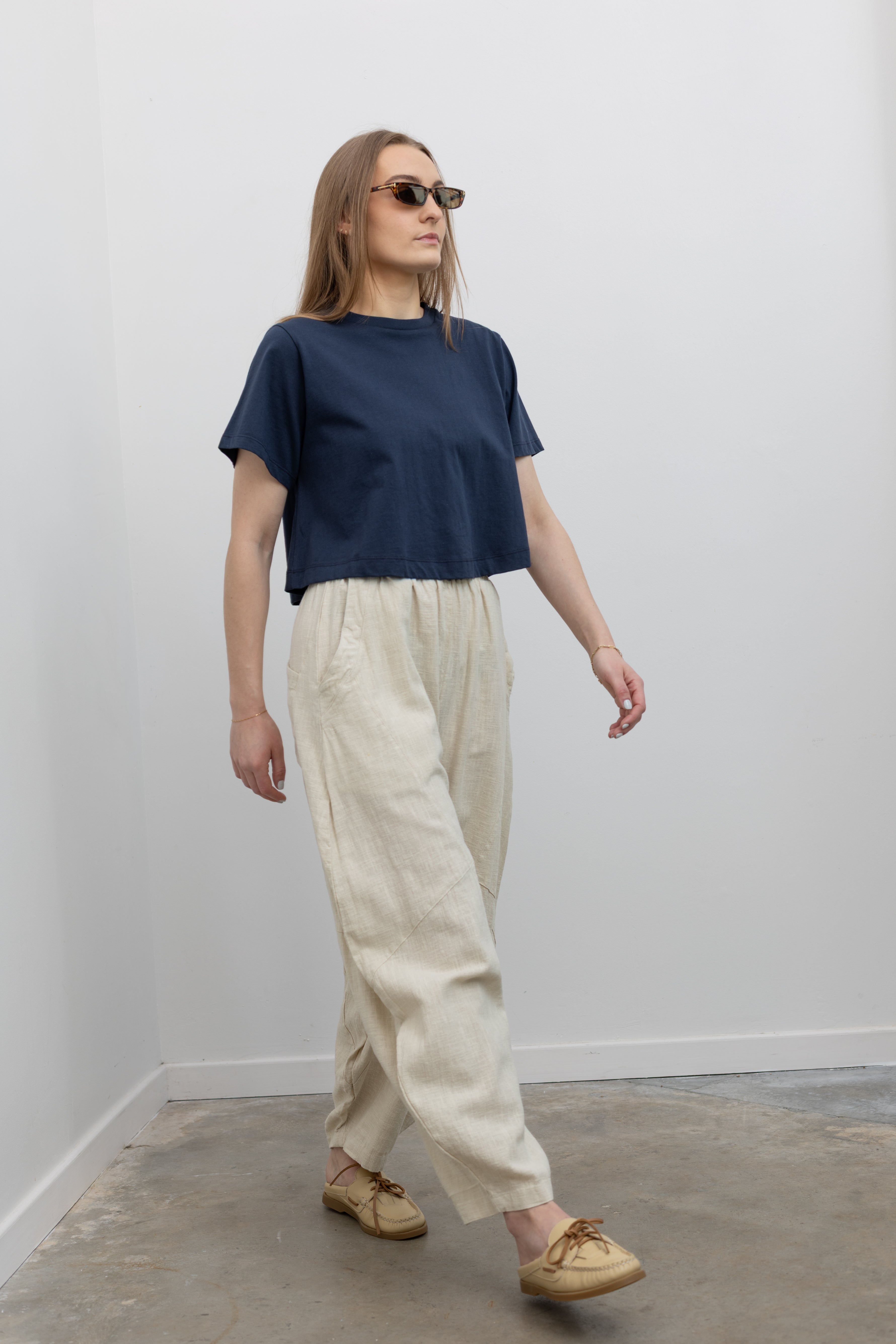 Woman walking wearing Spring fashion in an Alas Eius label navy blue crop top with a pair of Collective Linen Barrel Cotton Blend Pants and leather mule shoes at Alas Eius 