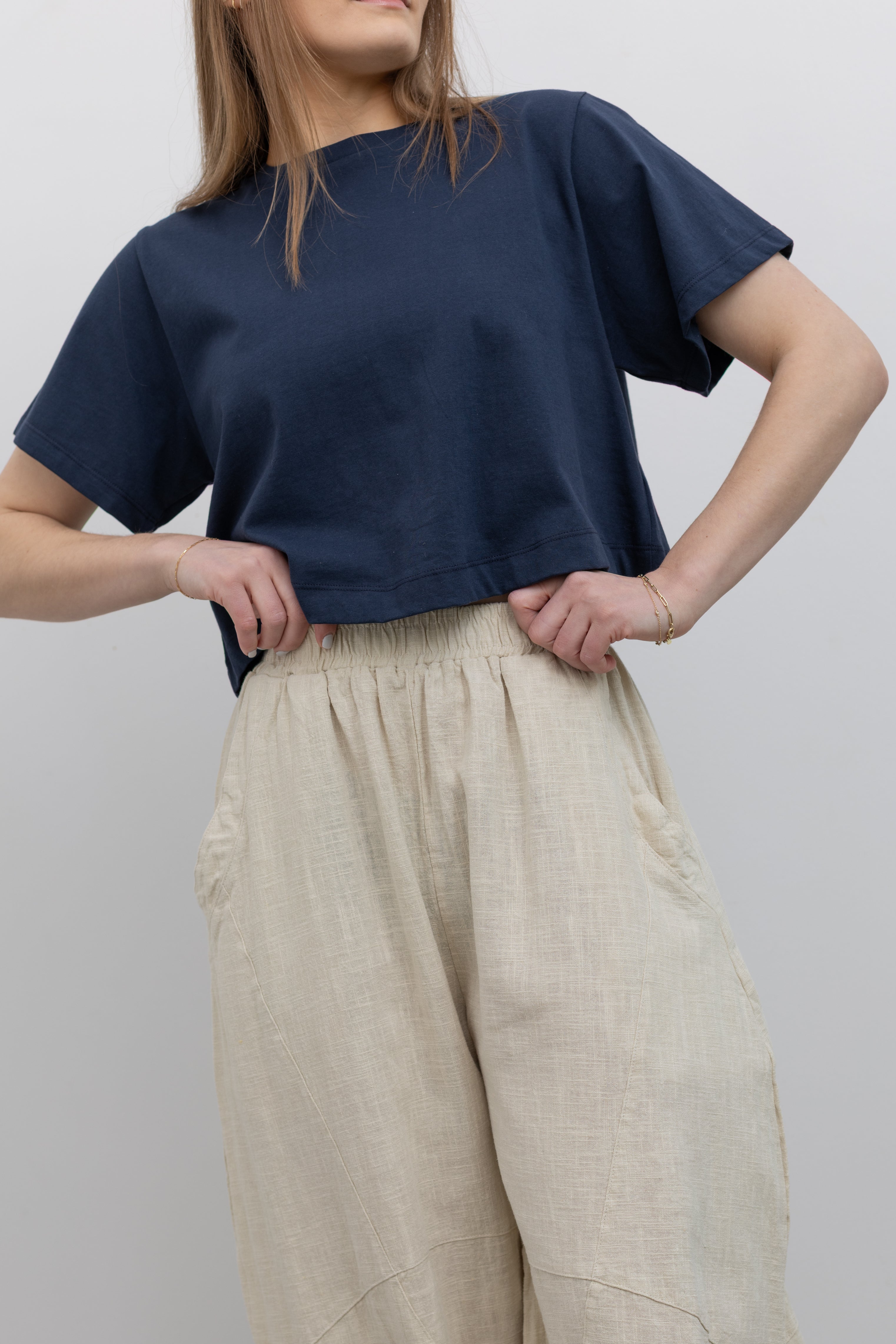 Product view of woman standing wearing Spring fashion in an Alas Eius label navy blue crop top with a pair of Collective Linen Barrel Cotton Blend Pants and leather mule shoes at Alas Eius 
