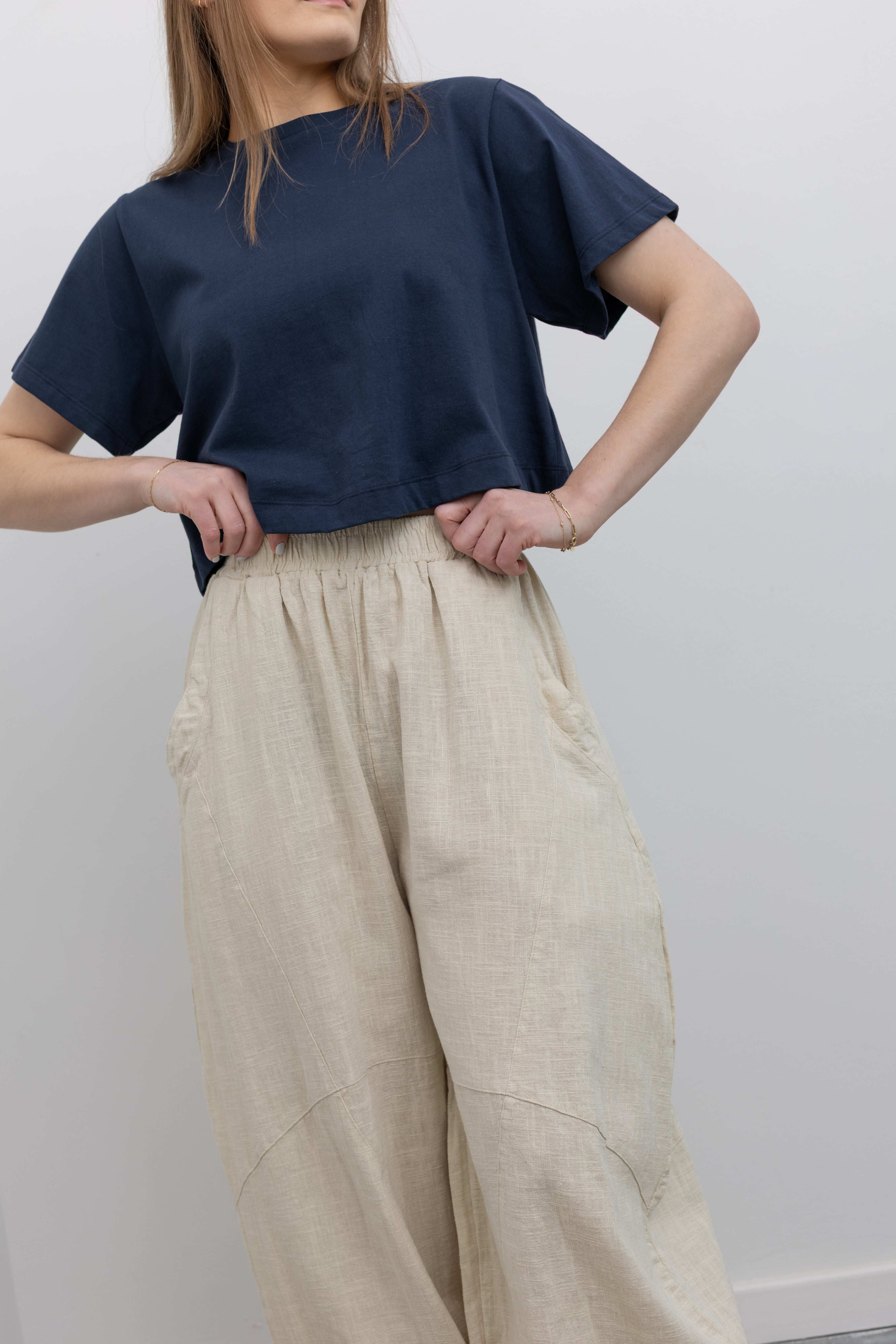 Product view of woman standing wearing Spring fashion in an Alas Eius label navy blue crop top with a pair of Collective Linen Barrel Cotton Blend Pants and leather mule shoes at Alas Eius 