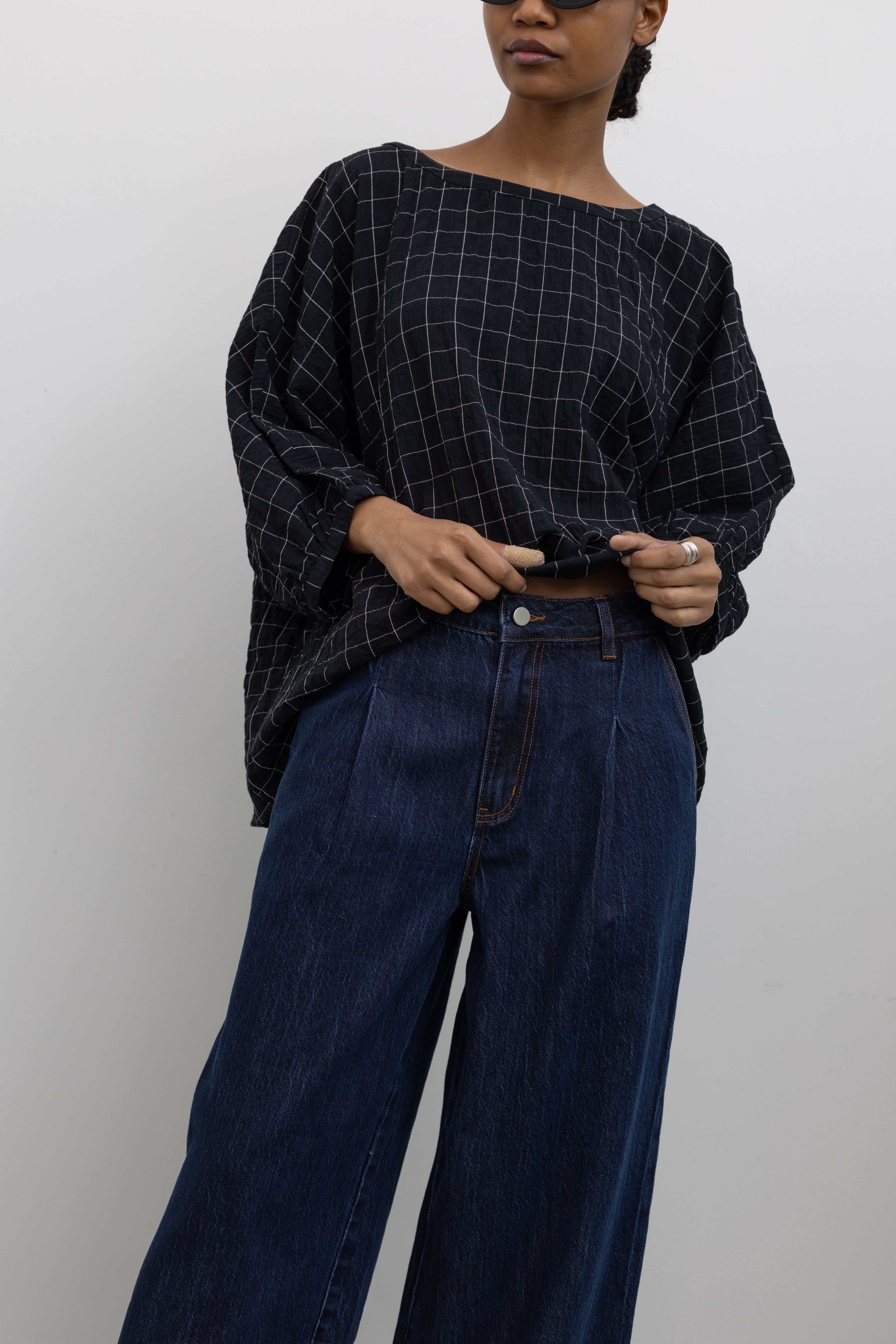 Close-up detailed view of a woman standing wearing a classic wardrobe staple in a pair of Collective indigo denim wide leg pleated jeans with a black top and black leather loafers at Alas Eius.