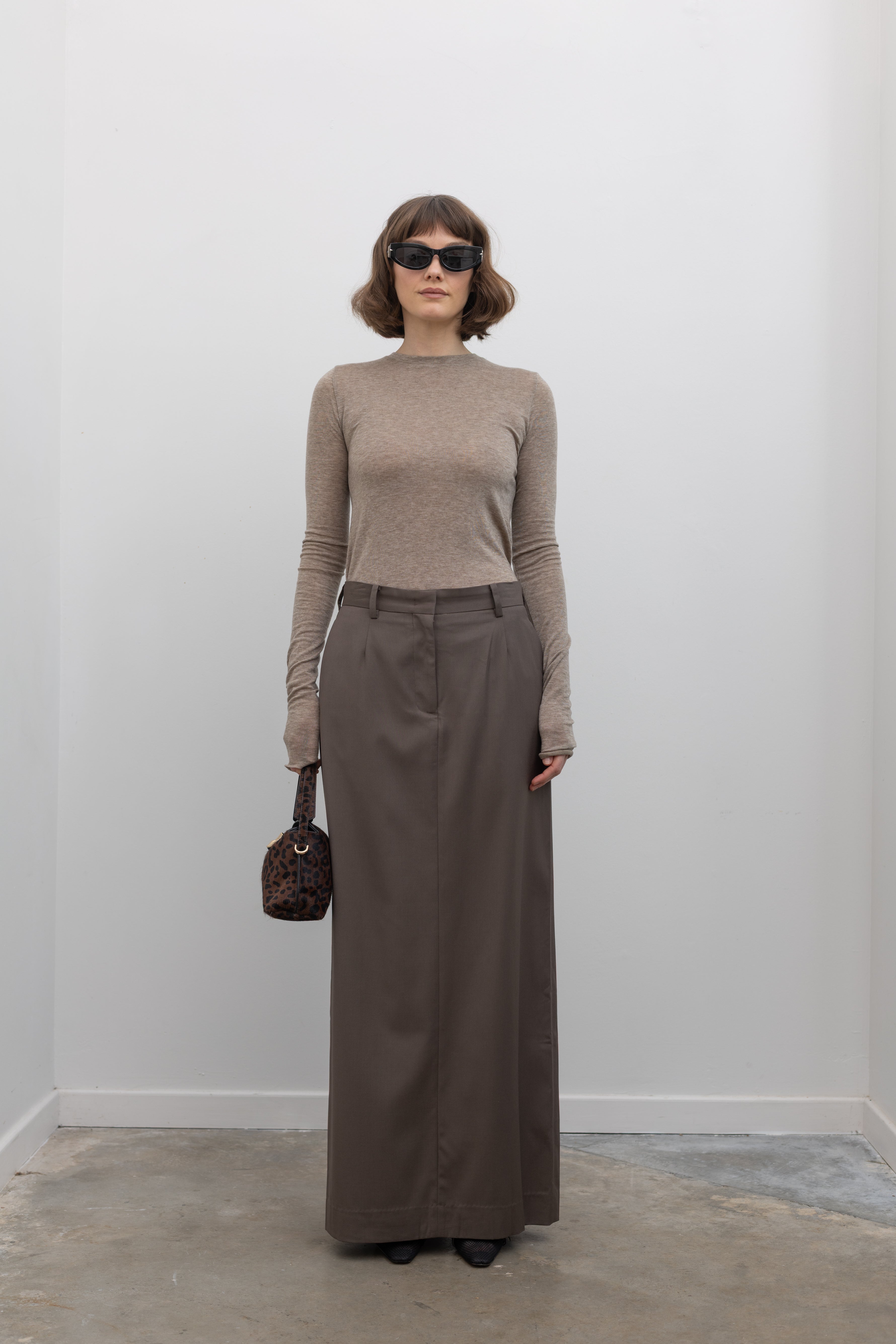 Close-up front view of a woman wearing an elevated capsule wardrobe essential in a Collective Brand Beige Merino Wool Long Sleeve Fitted Top paired with maxi skirt at Alas Eius. 