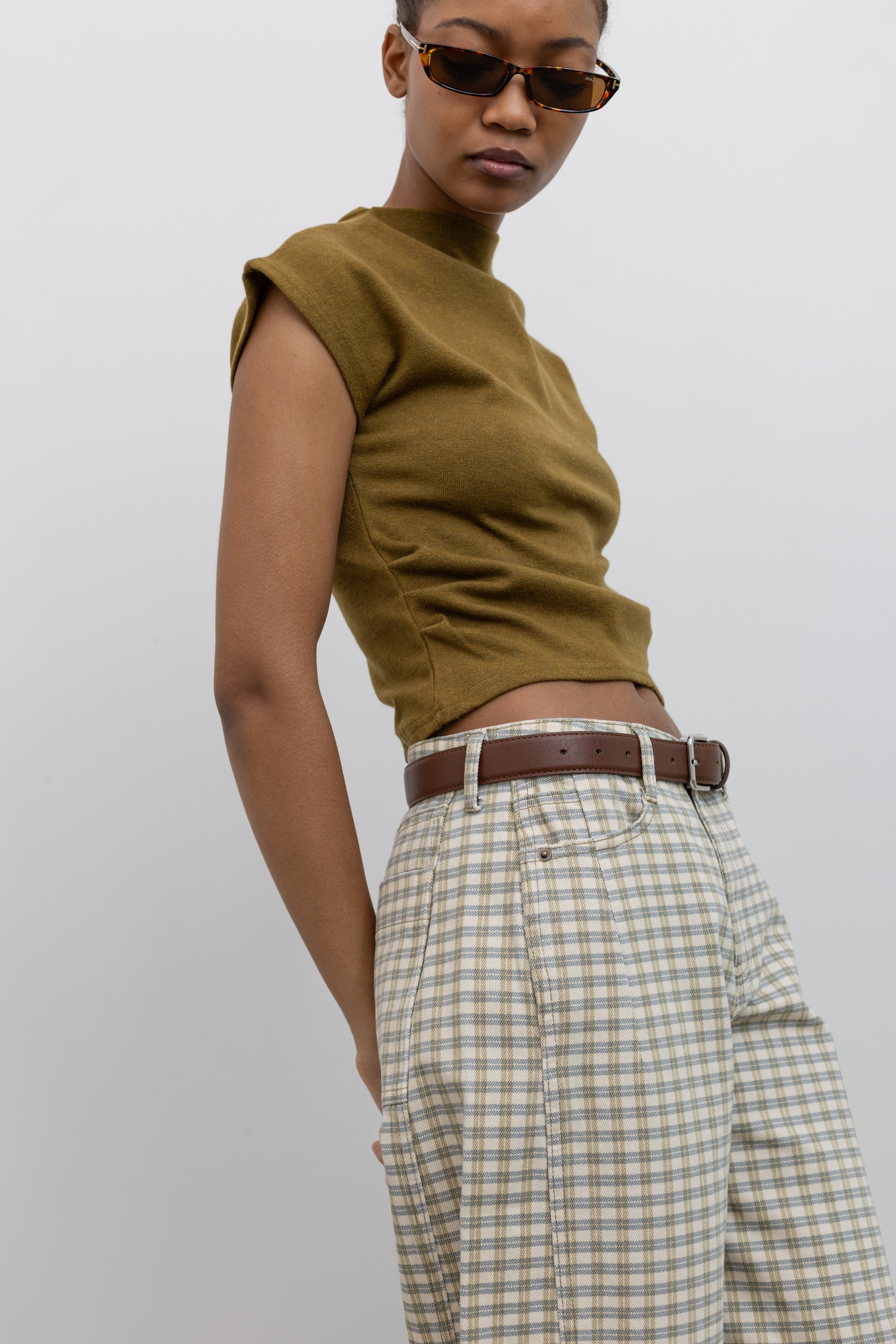 Side view of a woman wearing a capsule wardrobe essential accessory in a Collective brand classic brown leather belt made with a silver square shaped buckle at an Alas Eius store. 