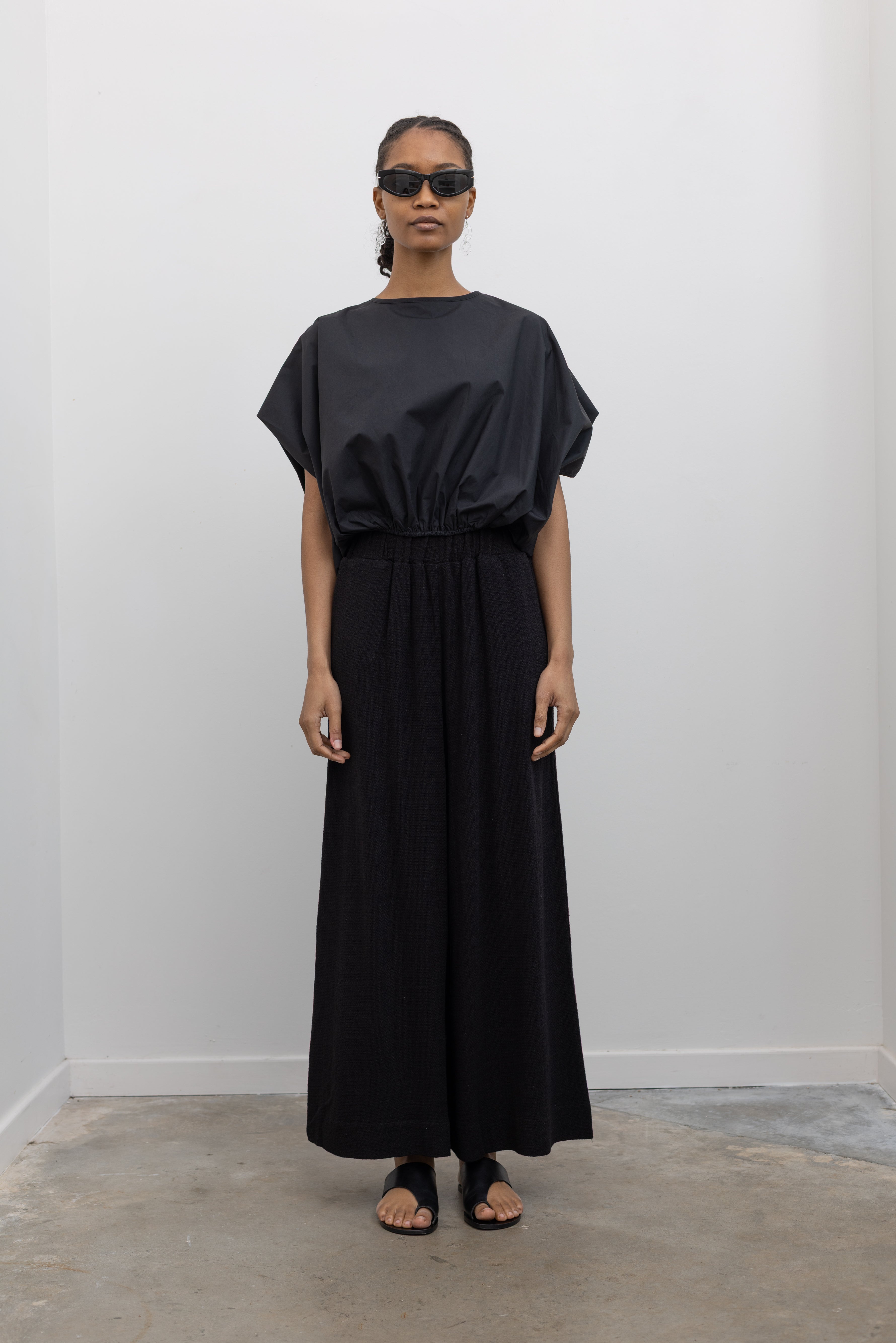 Full length front view of a woman posing wearing flattering and modest spring fashion in the Collective brand black linen wide leg pull on pants with pockets paired with a black balloon hem top and ATP black leather cutout sandals at an Alas Eius store. 