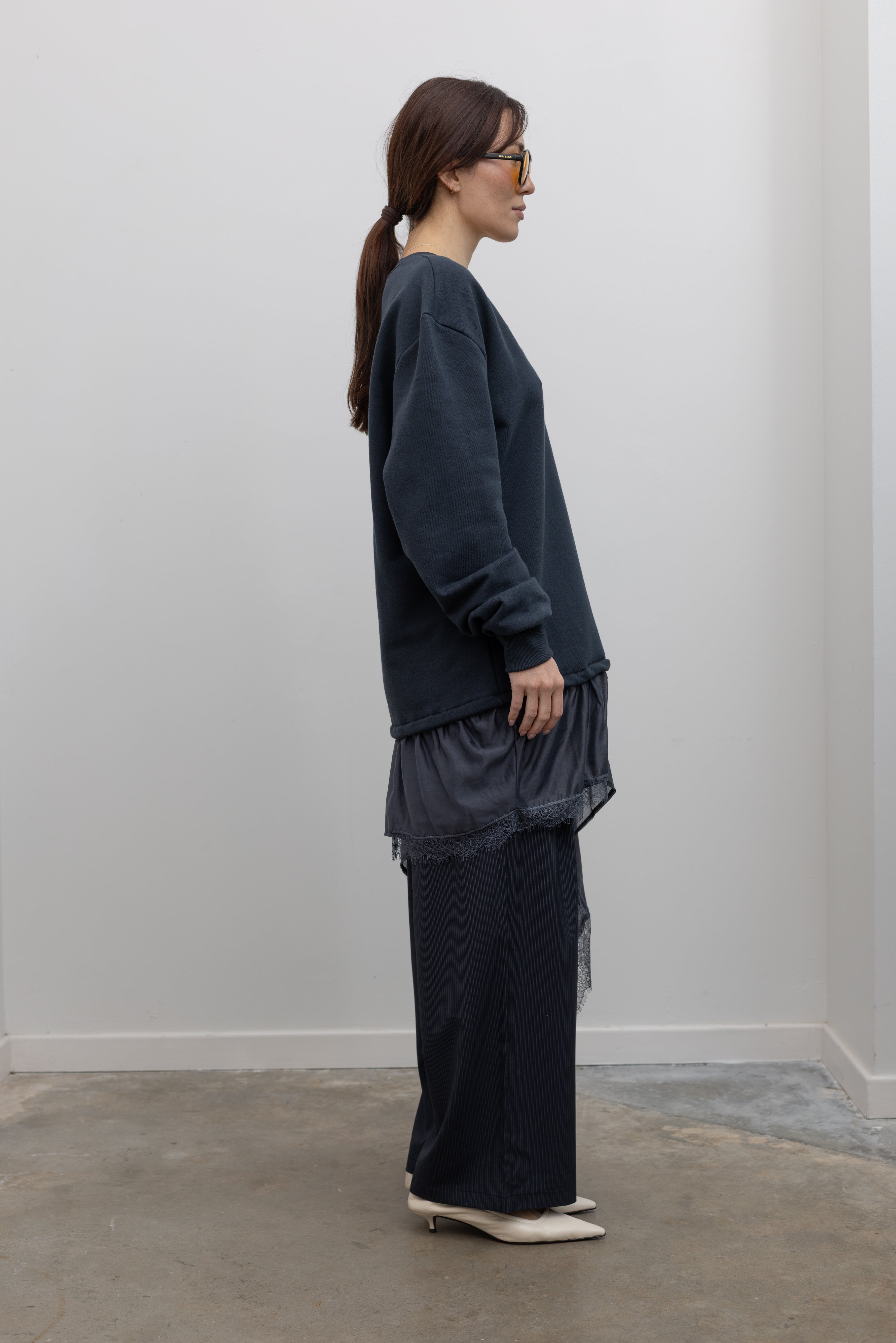 Side view of Woman wearing Spring fashion in a Collective Navy Lace Trim Cotton Oversized Jumper and navy blue pinstripe trousers with sunglasses and white pumps at Alas Eius 