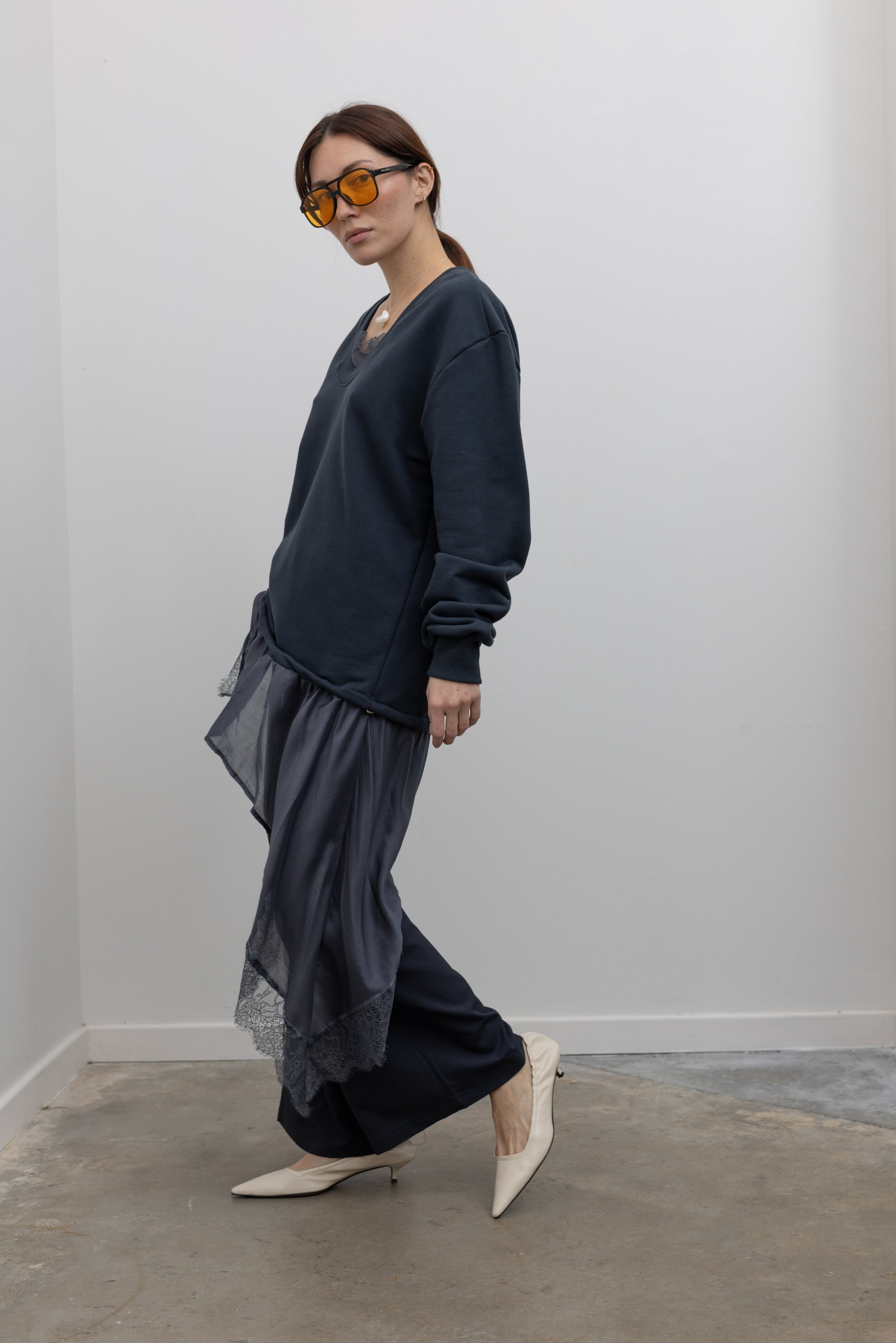 Side view of Woman standing wearing Spring fashion in a Collective Navy Lace Trim Cotton Oversized Jumper and navy blue pinstripe trousers with sunglasses and white pumps at Alas Eius 