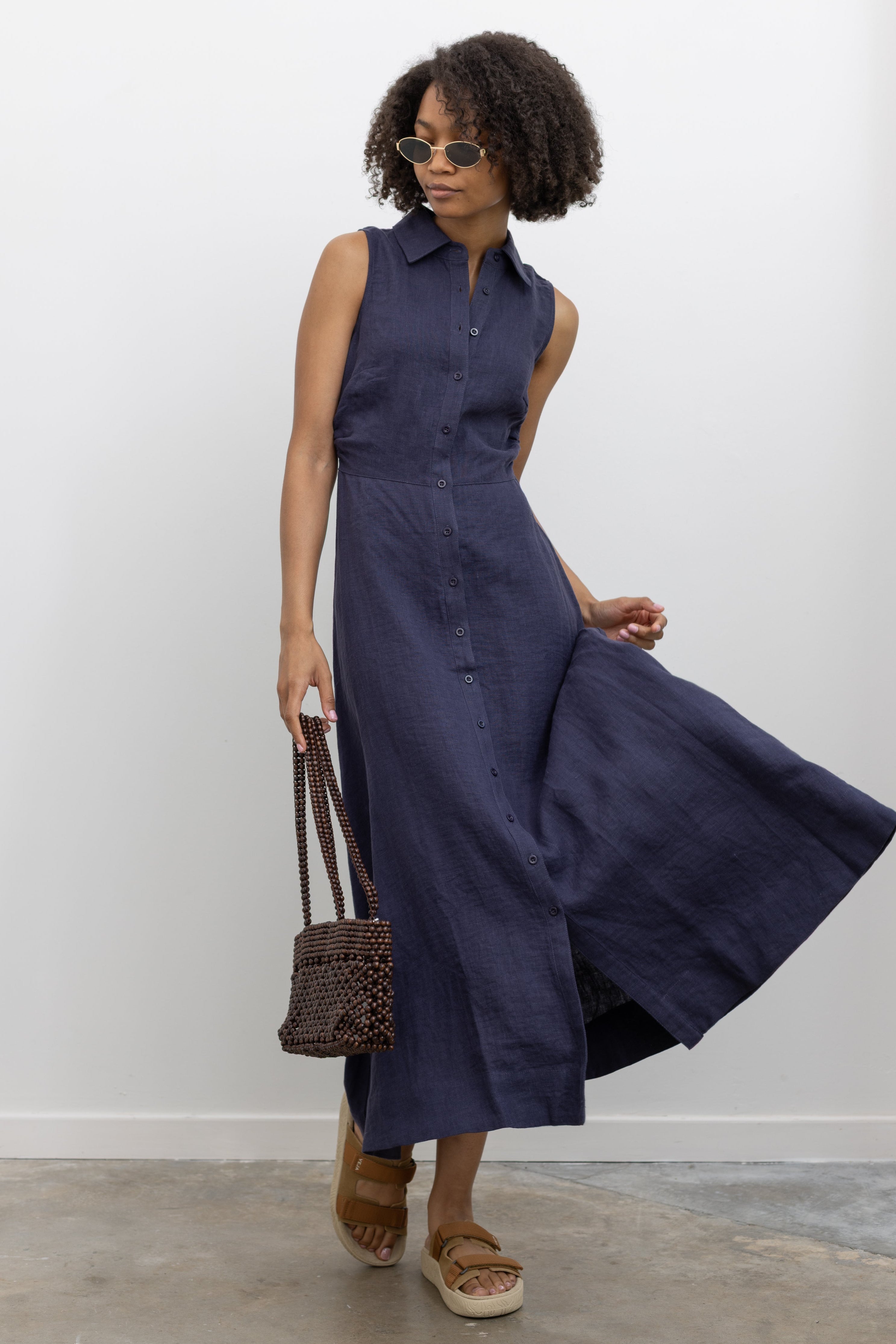 Woman in motion wearing chic summer fashion in a Collective navy blue linen midi length collared shirt dress with buttons down the front paired with Veja slide sandals at Alas Eius 