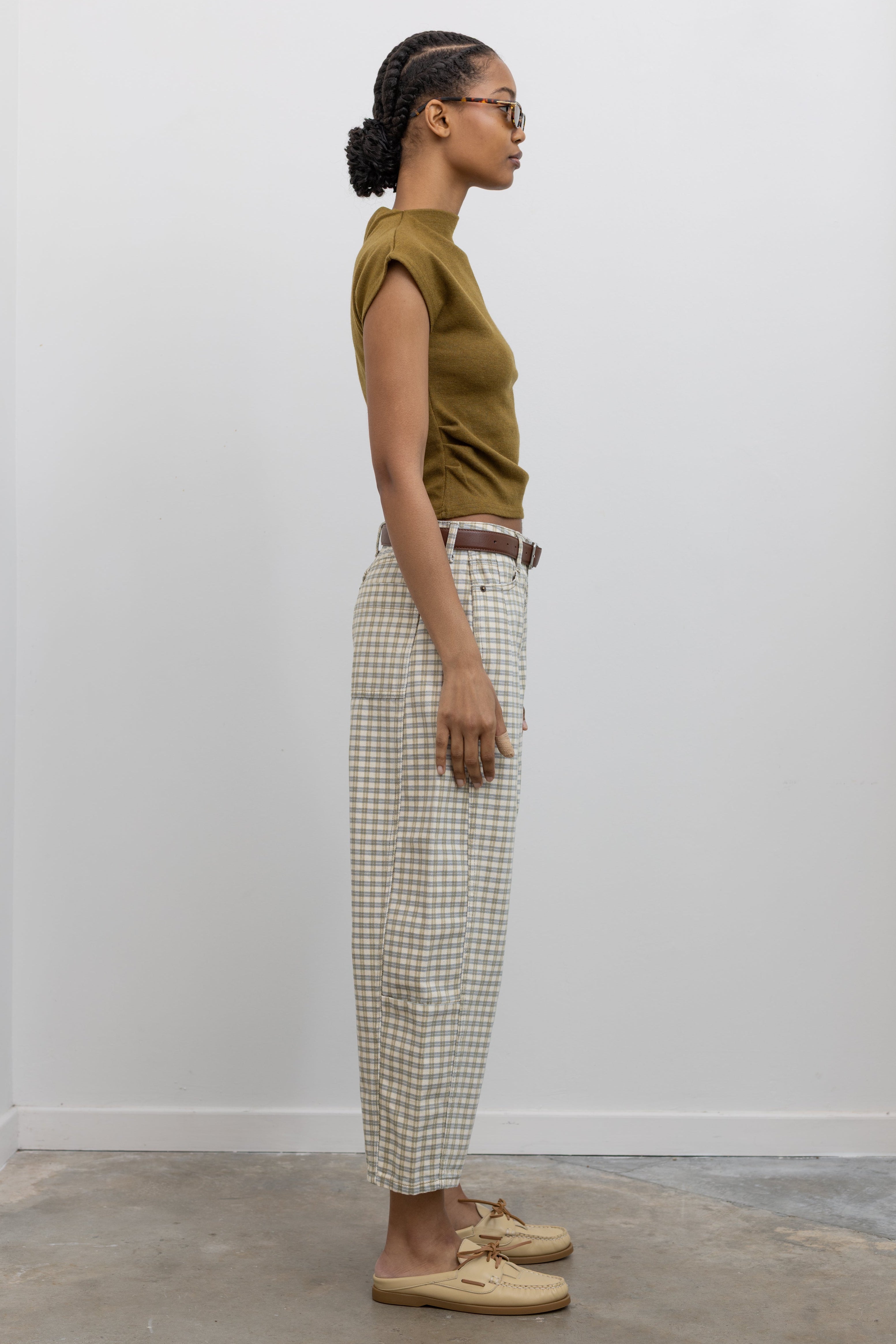 Side view of a woman standing wearing Spring fashion in a pair of Collective Olive Checkered Barrel Cropped Pants with a short sleeved top and beige leather shoes at Alas Eius