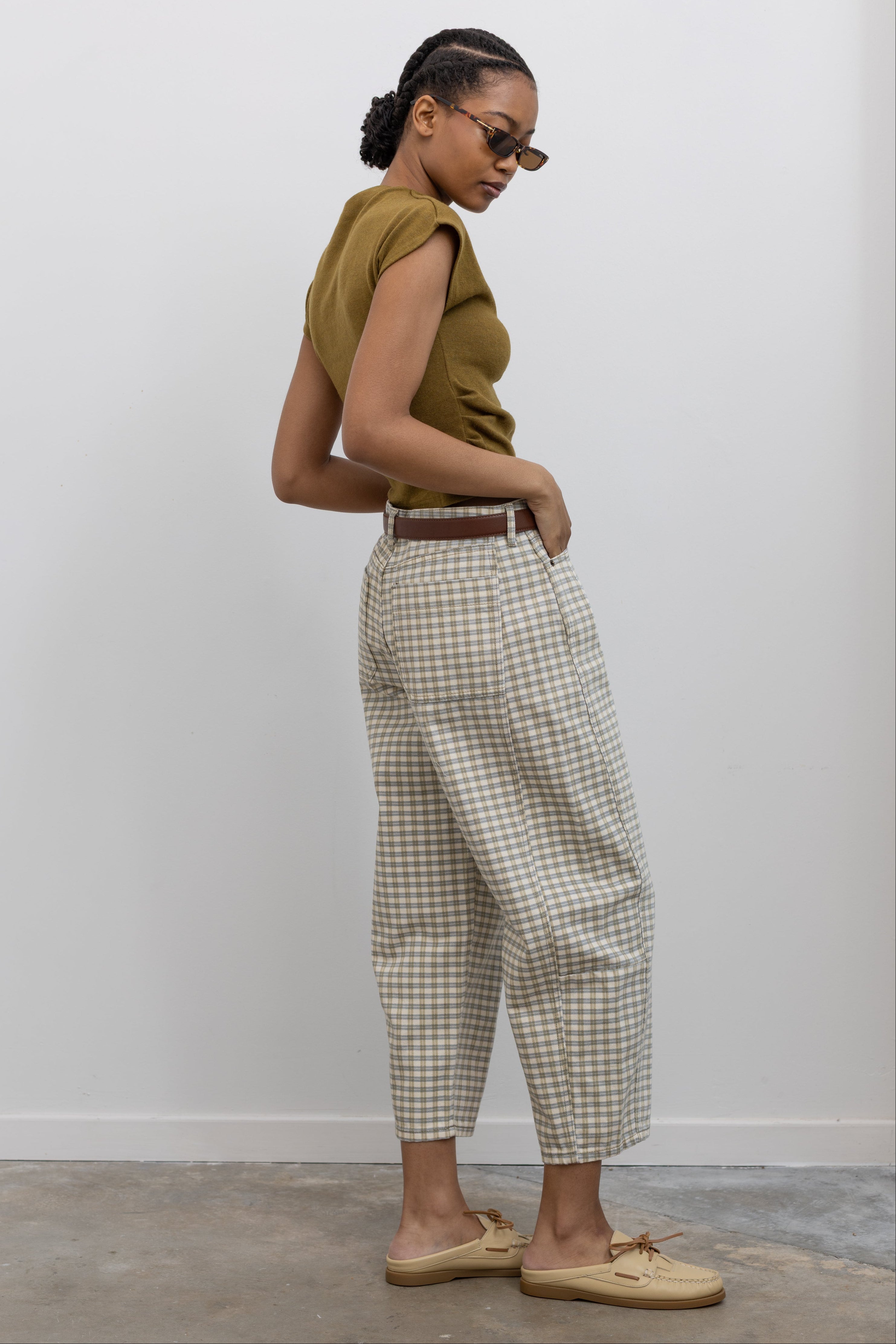 Side view of a woman posing wearing Spring fashion in a pair of Collective Olive Checkered Barrel Cropped Pants with a short sleeved top and beige leather shoes at Alas Eius 