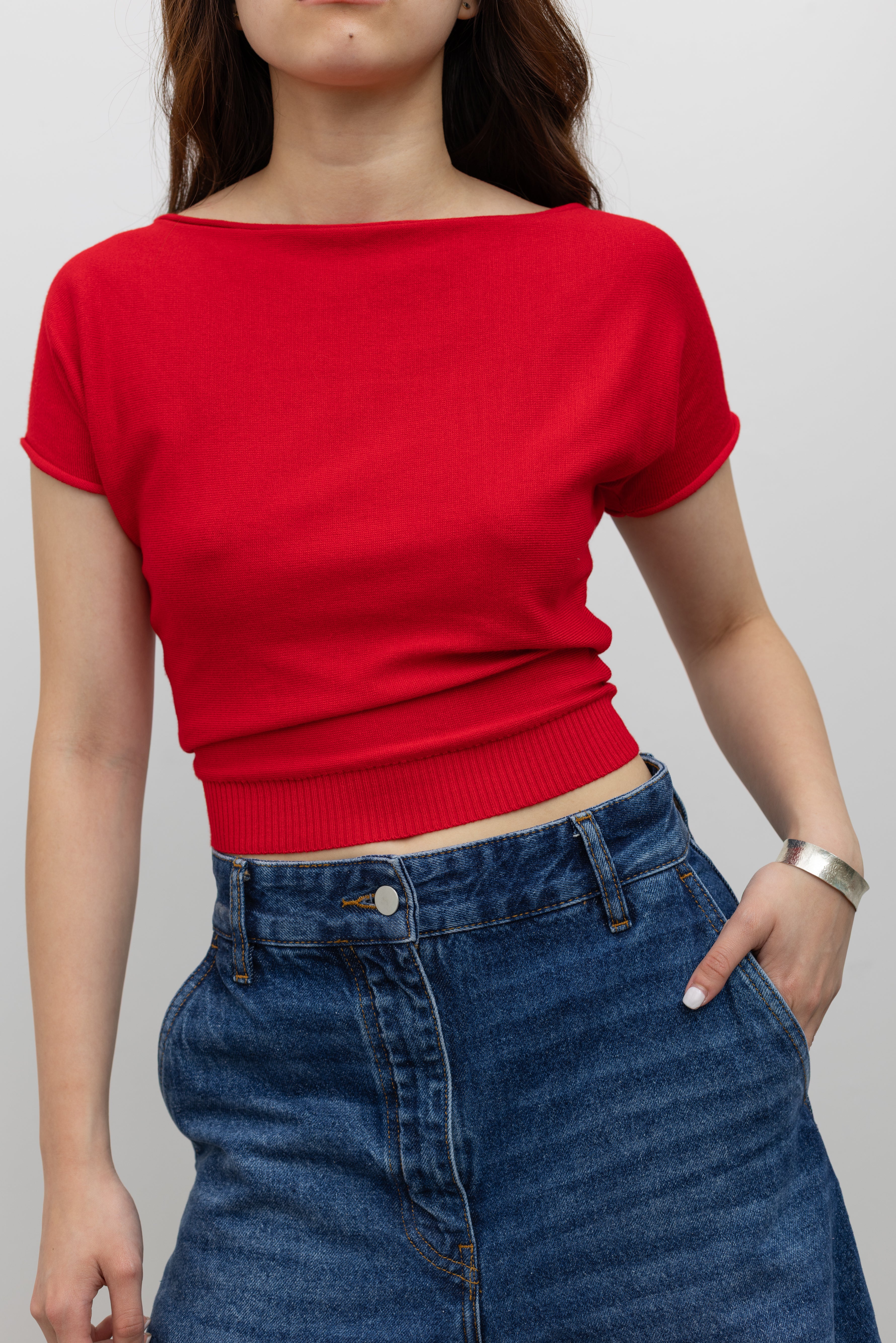 Woman wearing elevated basic top in a Collective red knit short sleeve fitted crop top with a boat neck paired with Studio Nicholson wide crop denim jeans at Alas Eius. 