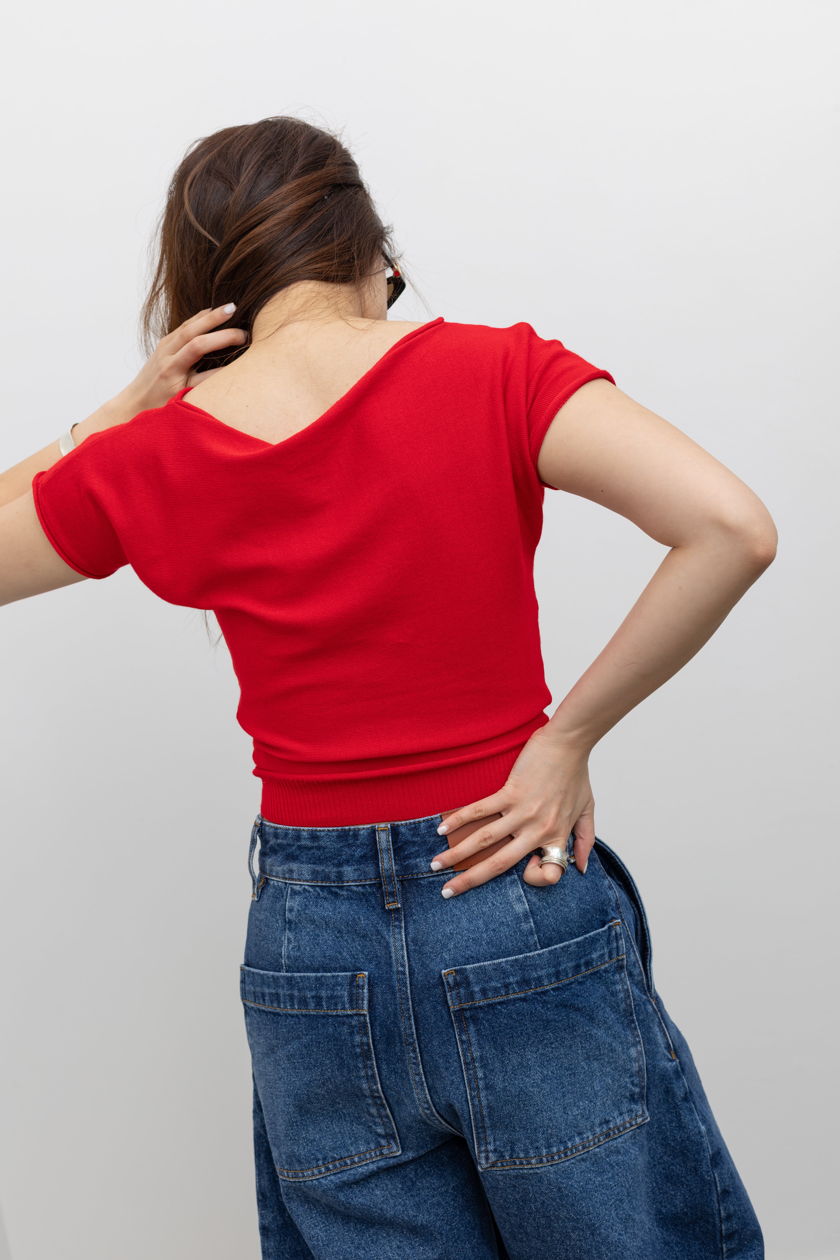 Back view of a woman wearing elevated basic top in a Collective red knit short sleeve fitted crop top with Studio Nicholson wide crop denim jeans at Alas Eius. 