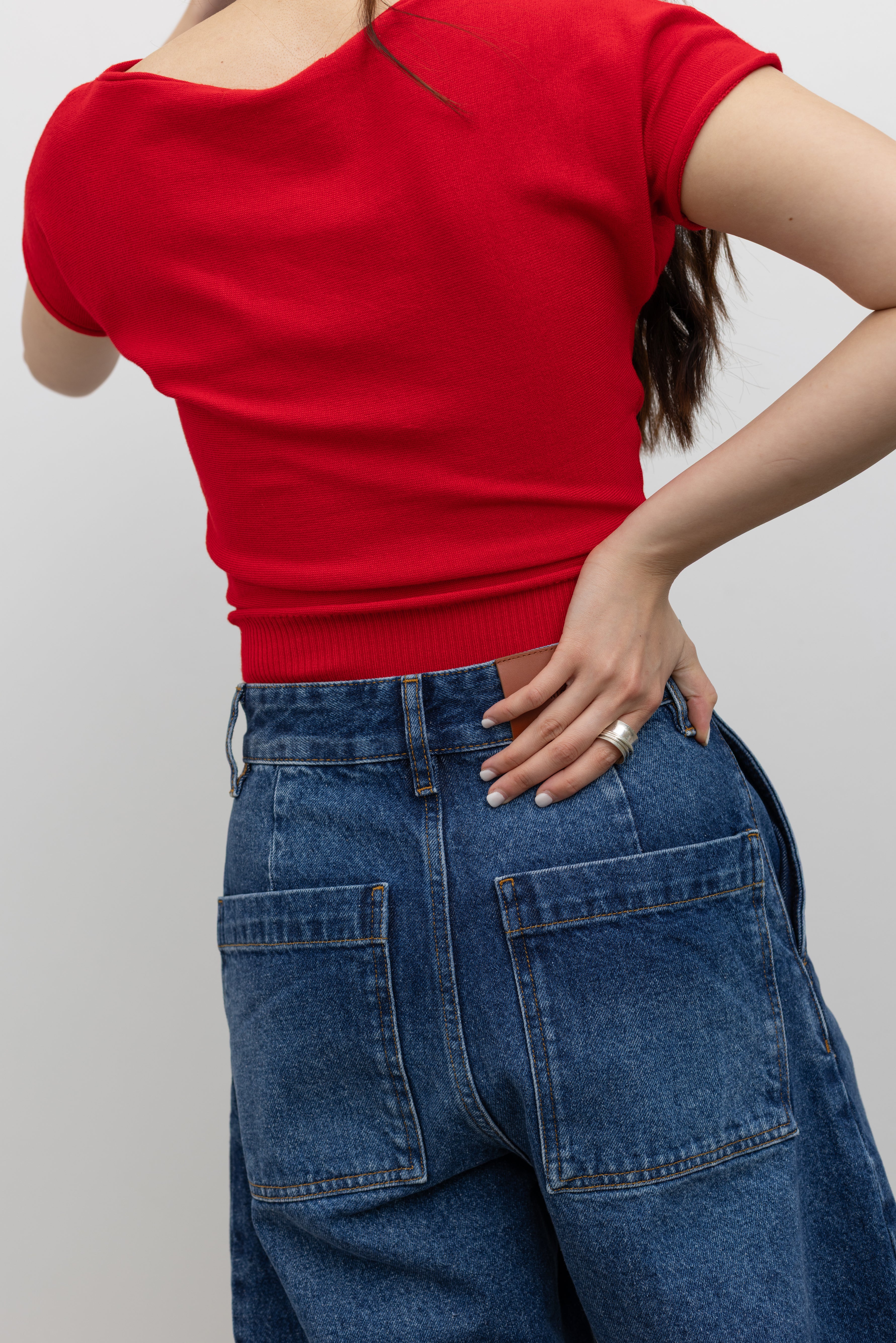 Back view of a woman wearing elevated basic top in a Collective red knit short sleeve fitted crop top with Studio Nicholson wide crop denim jeans at Alas Eius. 