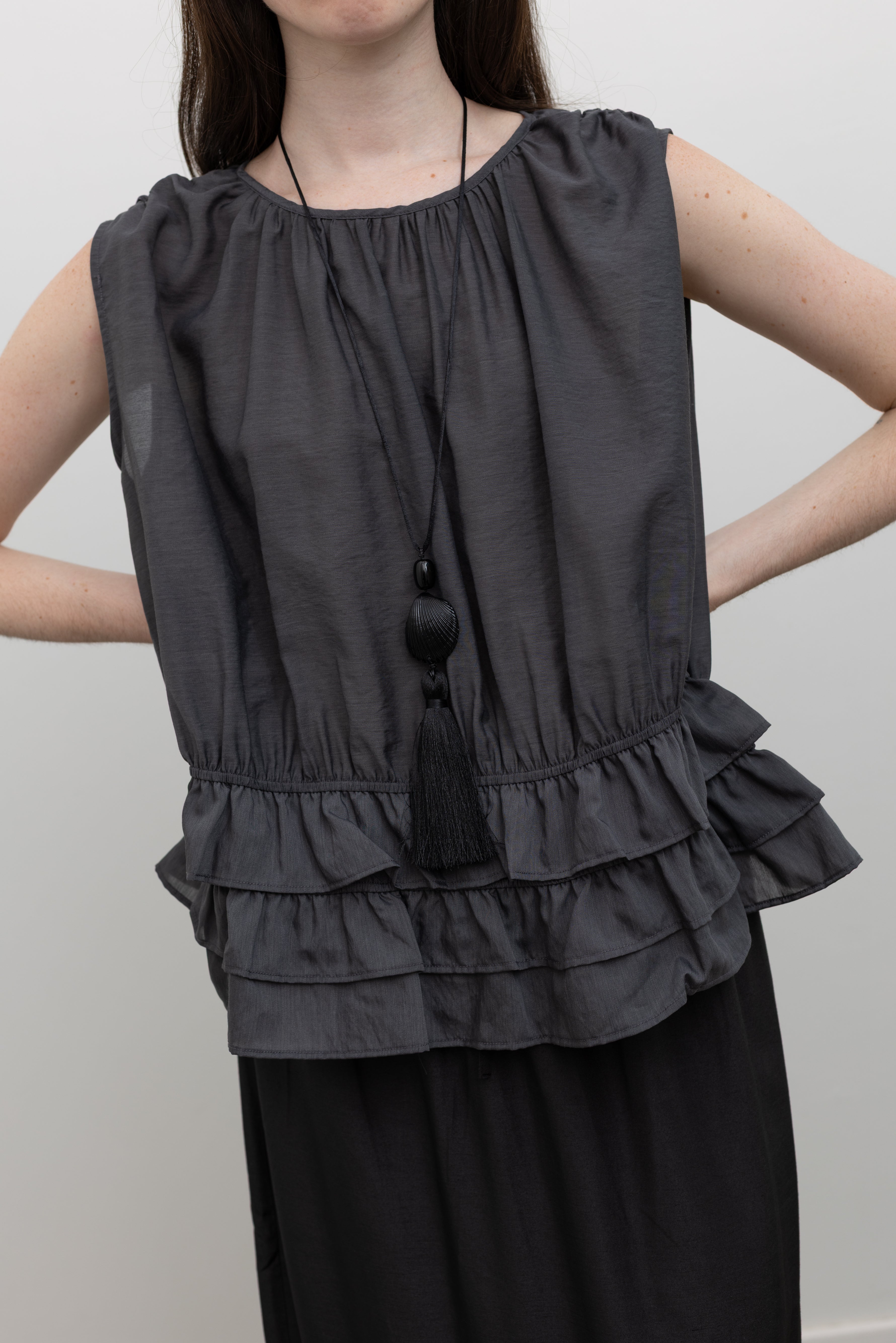 Collective sleeveless Tencel blouse featuring shirred waist definition, tiered ruffle hem, and elegant gathered neckline designed for refined minimalist womenswear at Alas Eius