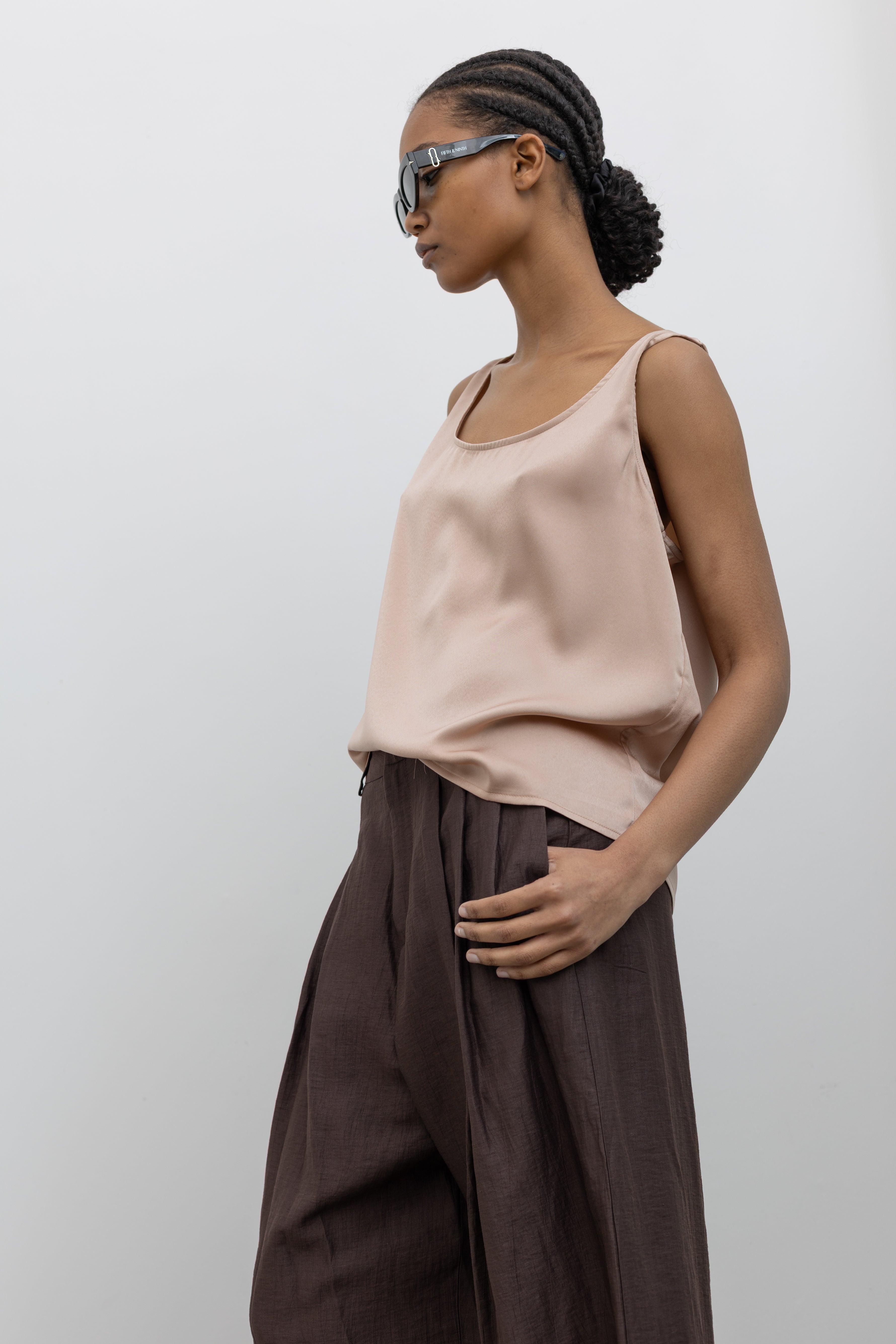 3/4 view of a woman wearing Spring fashion in a Collective brand solid beige satin tank top with a relaxed flowy fit paired with pleated trouser at Alas Eius.