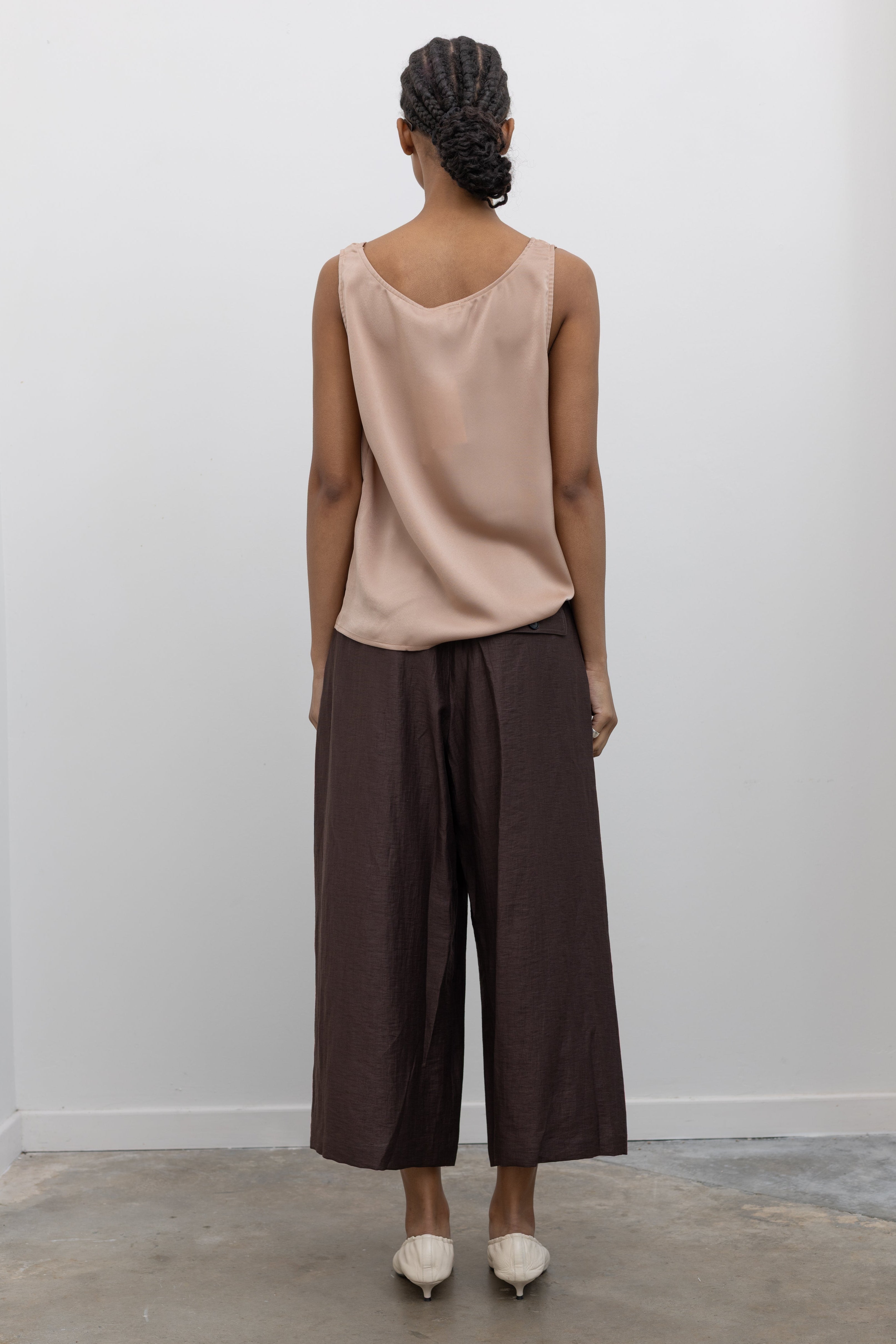 Full length back view of a woman wearing Spring fashion in a Collective brand solid beige satin tank top with a relaxed flowy fit paired with pleated trouser at Alas Eius.