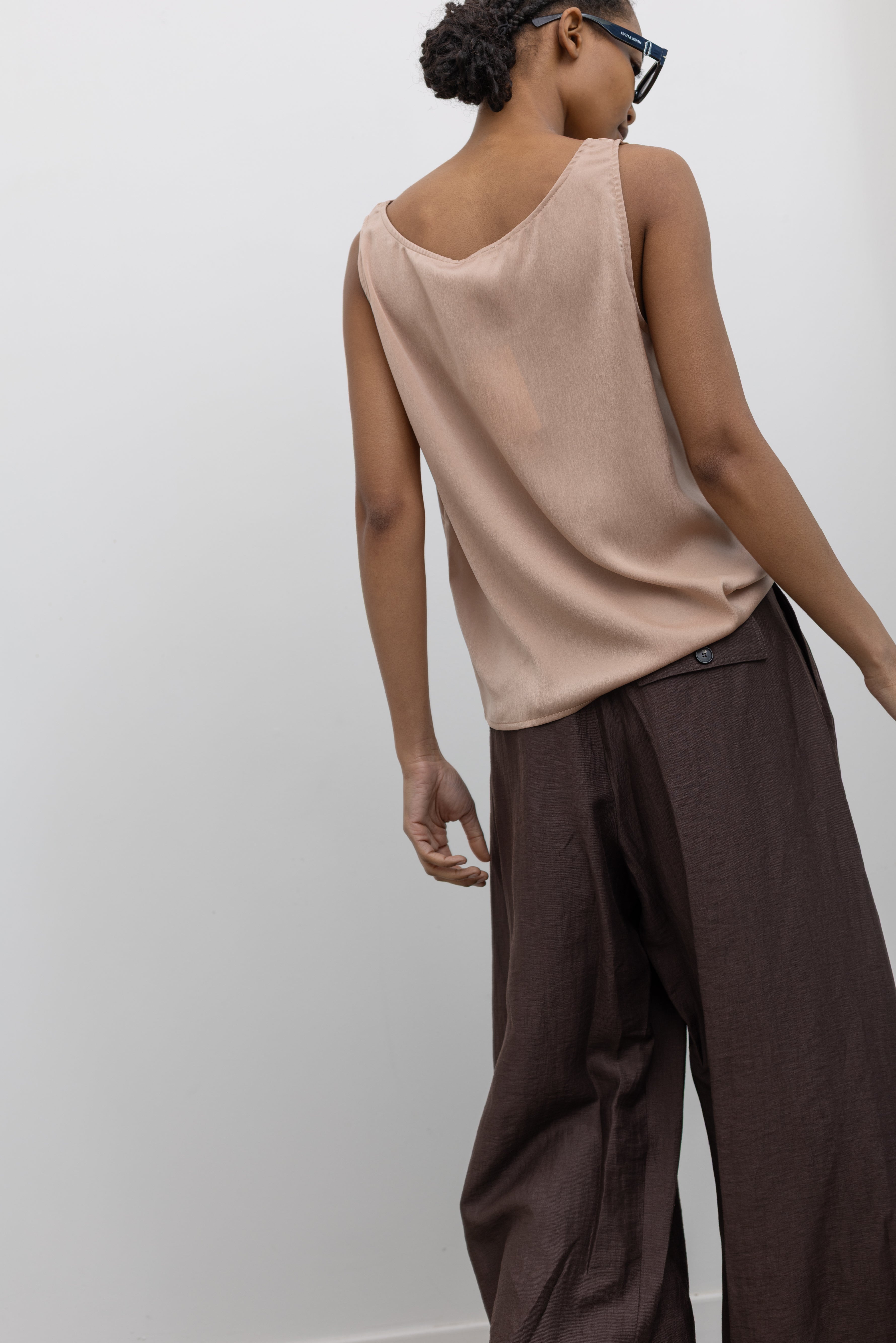 Back view of a woman in motion wearing Spring fashion in a Collective brand solid beige satin tank top with a relaxed flowy fit paired with pleated trouser at Alas Eius.